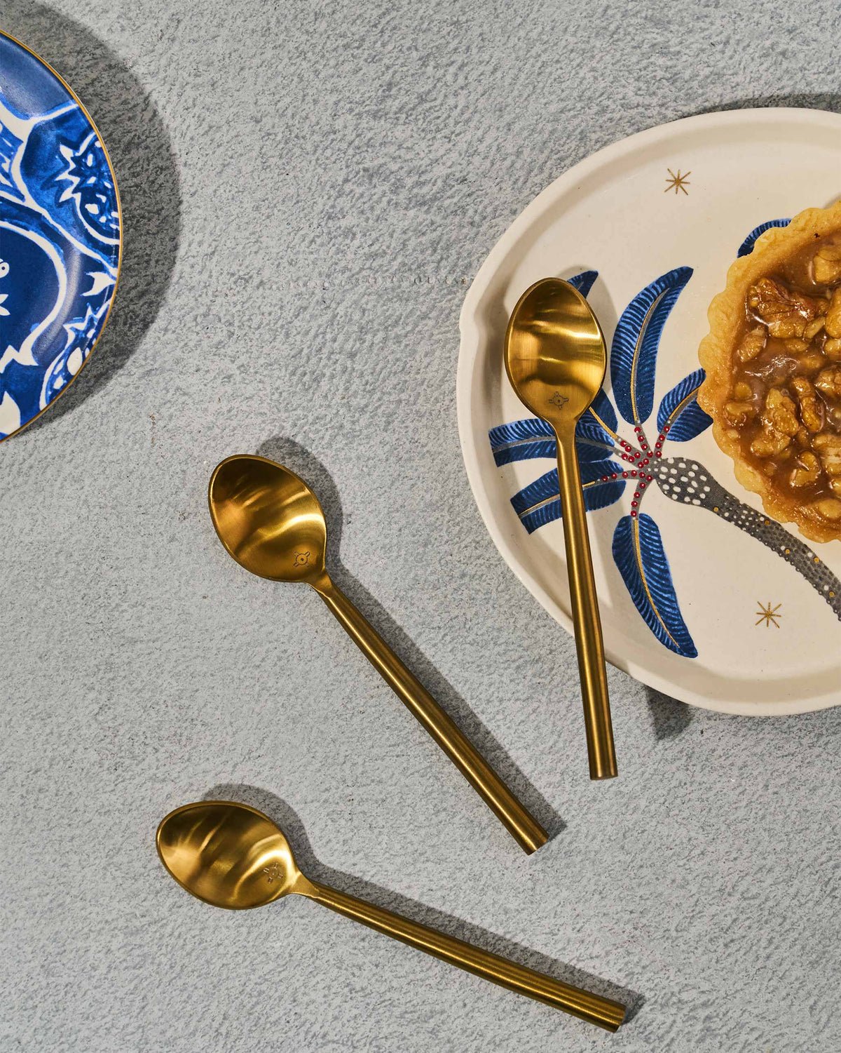 Gold Sahara dessert spoons beside a plate with a small tart.