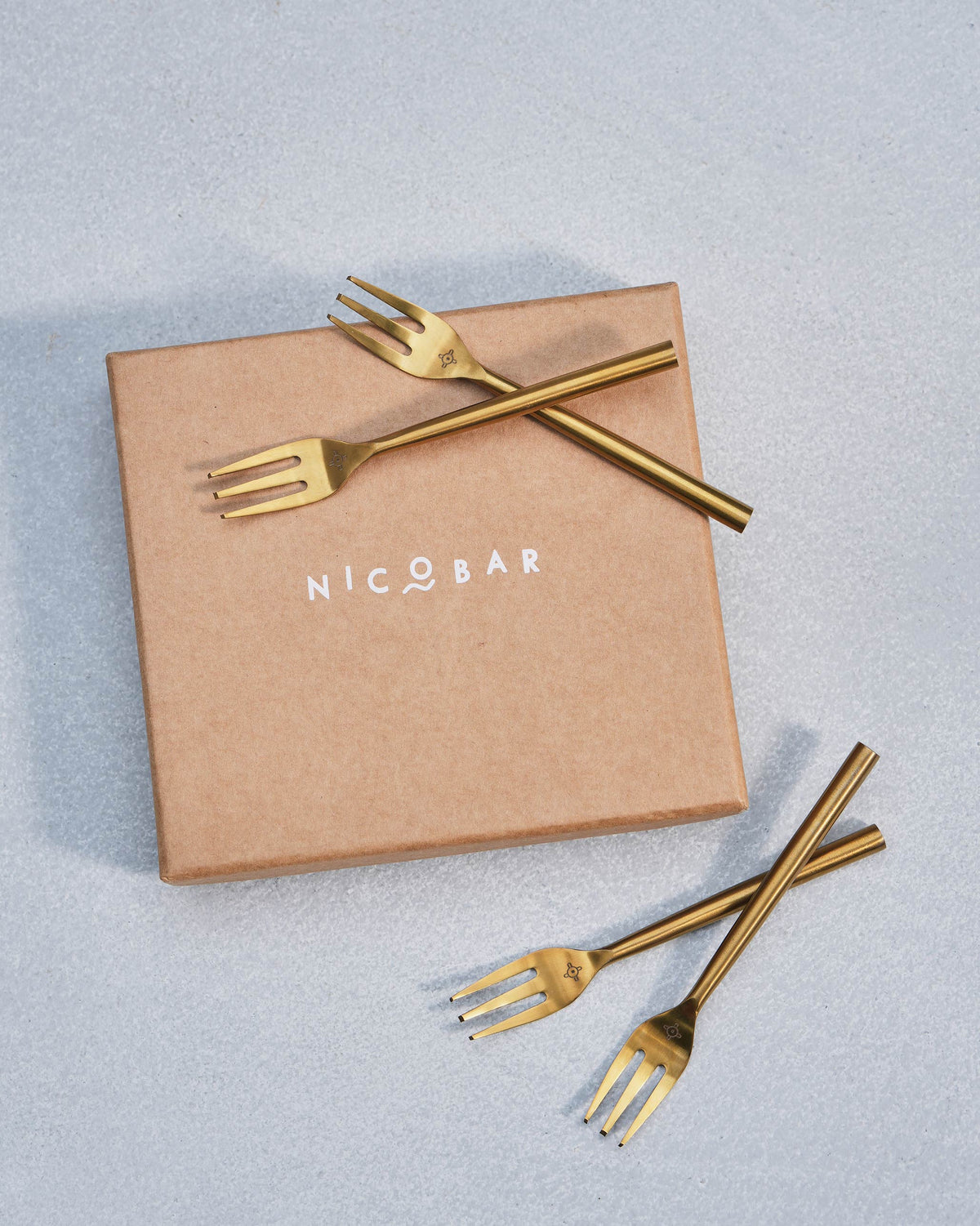 Gold Sahara dessert forks crossed over a Nicobar gift box.