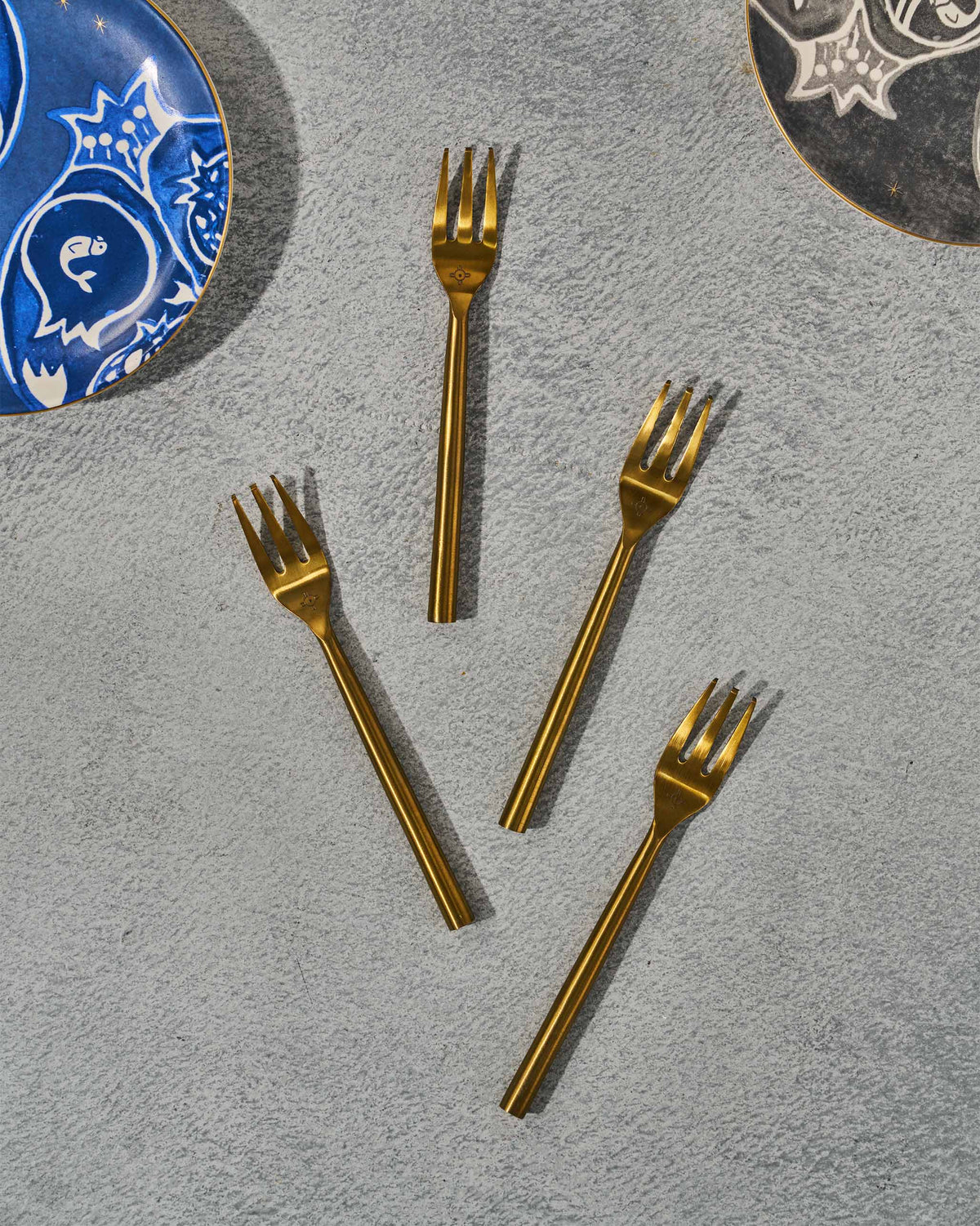 Four gold Sahara dessert forks between patterned plates on a table.