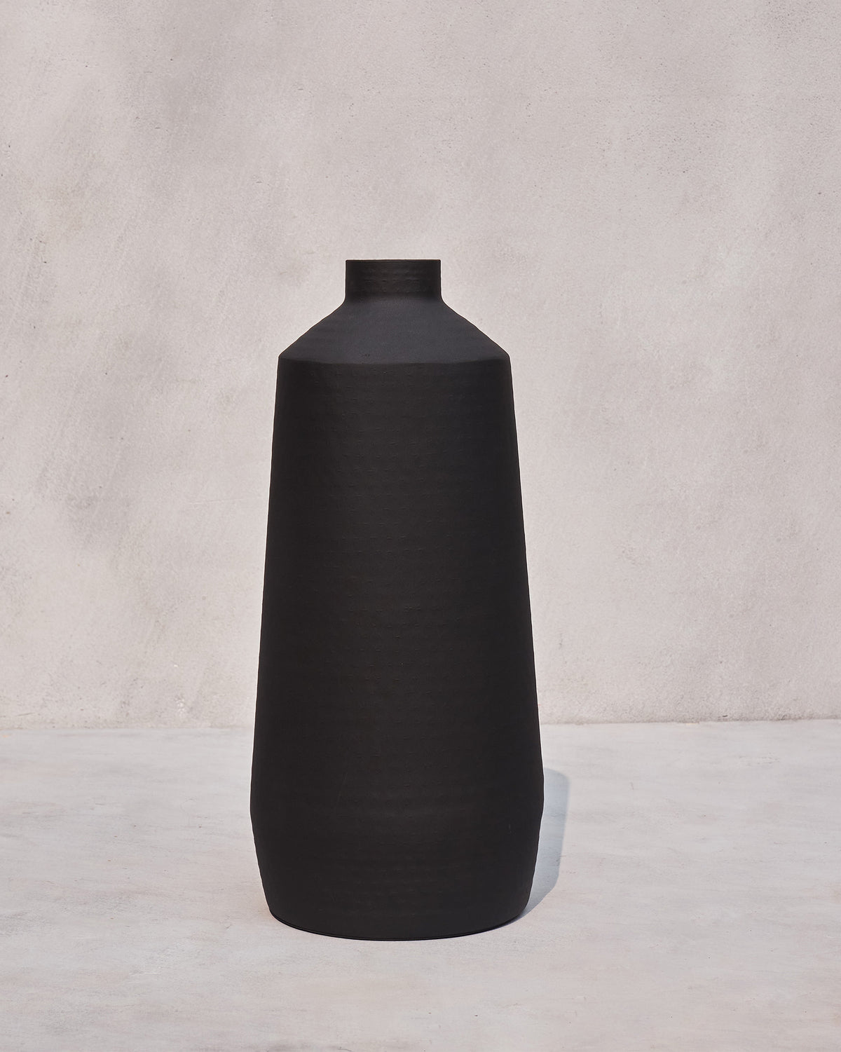 Nadi Vase - Large in matte black against a pale wall.