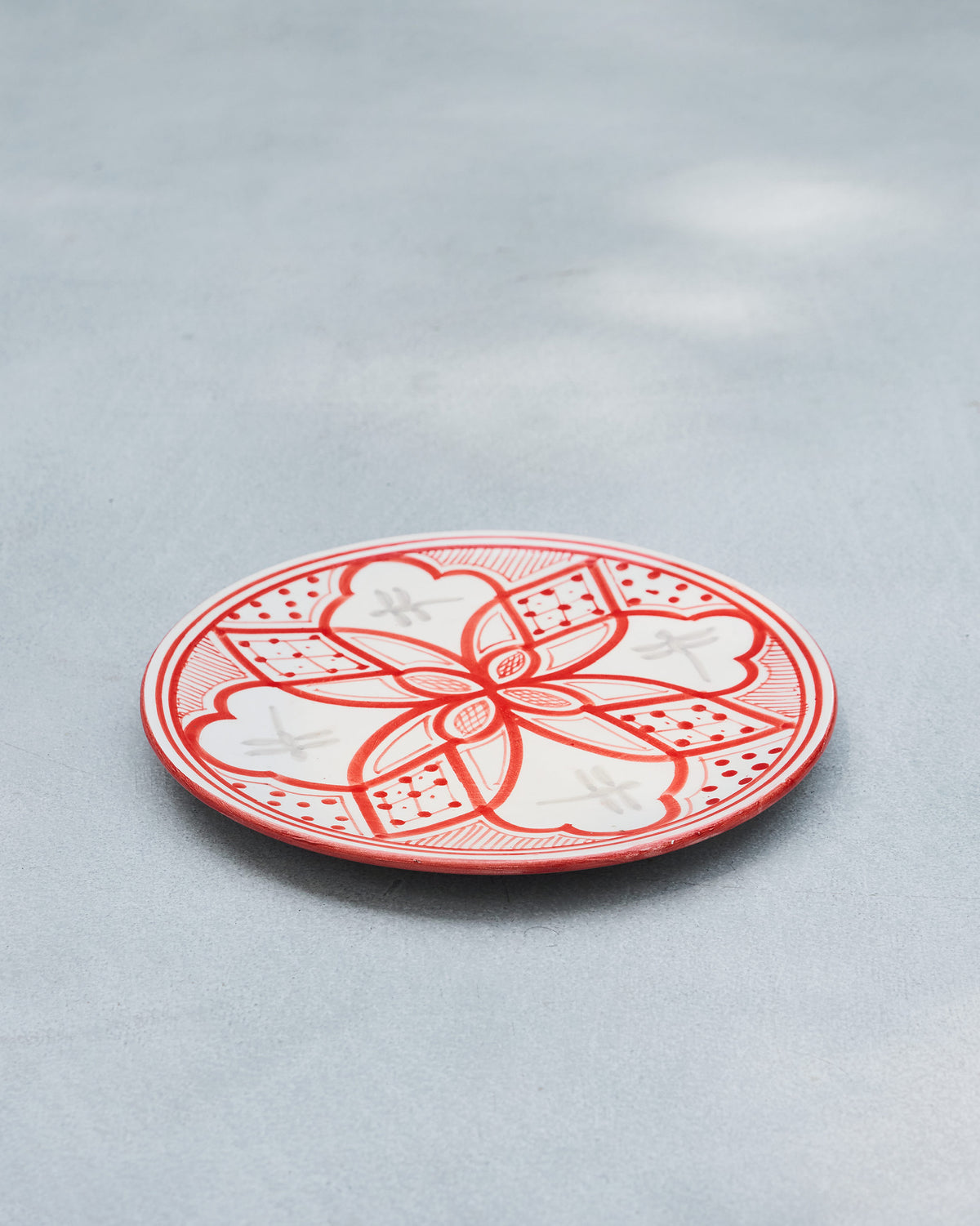 Angled view of a red Mosaic Oasis quarter plate with a geometric floral pattern.
