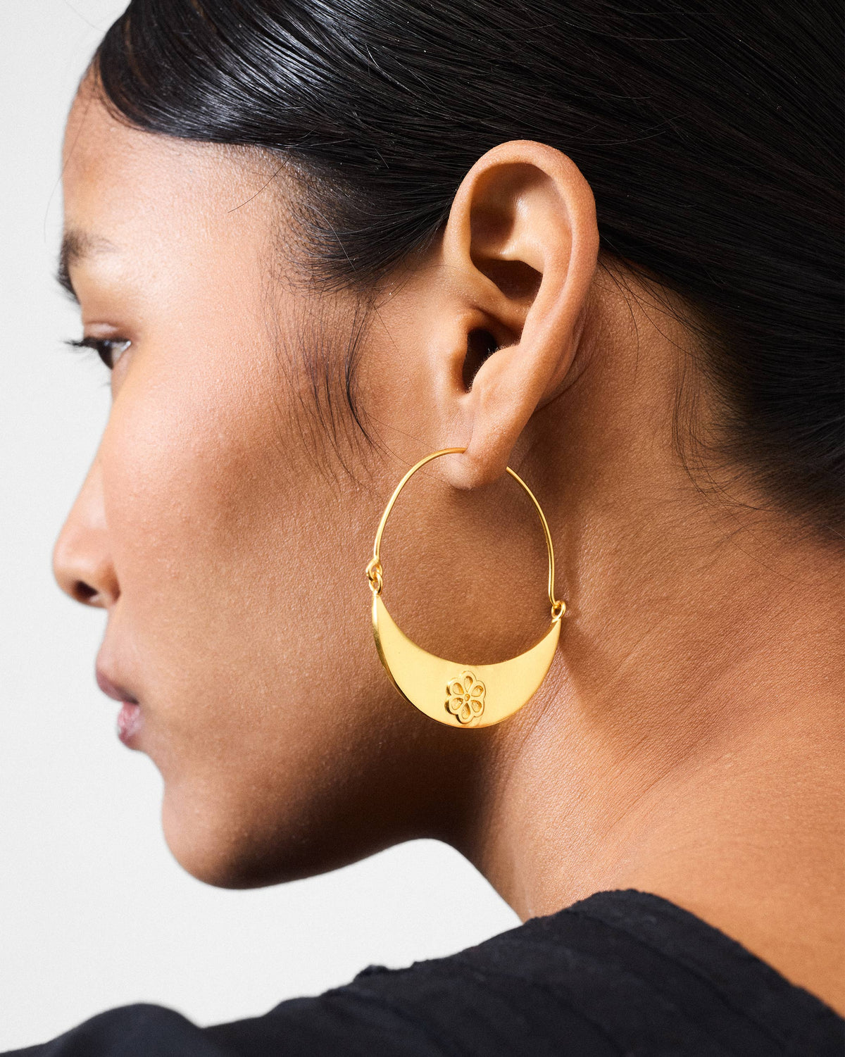 Side profile of a gold Boat bali with a floral crescent plate on a person.