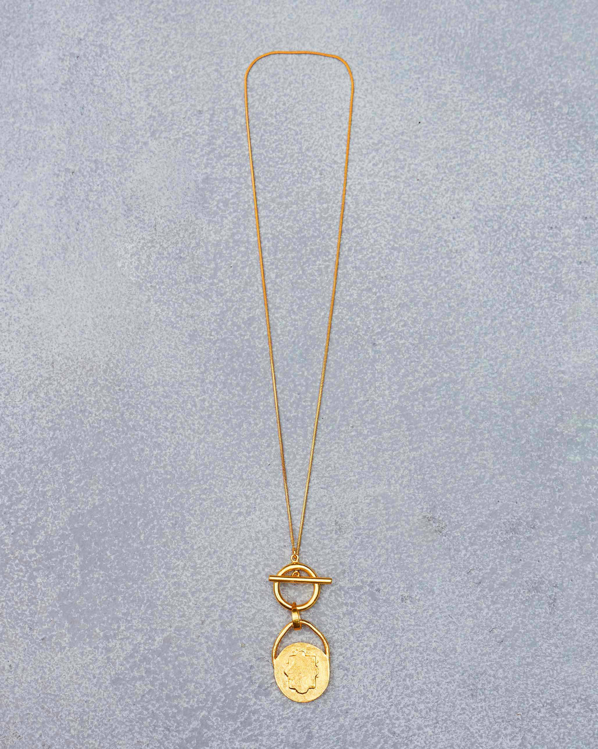 Long gold Stardrop Necklace laid flat, with a toggle clasp and medallion pendant.