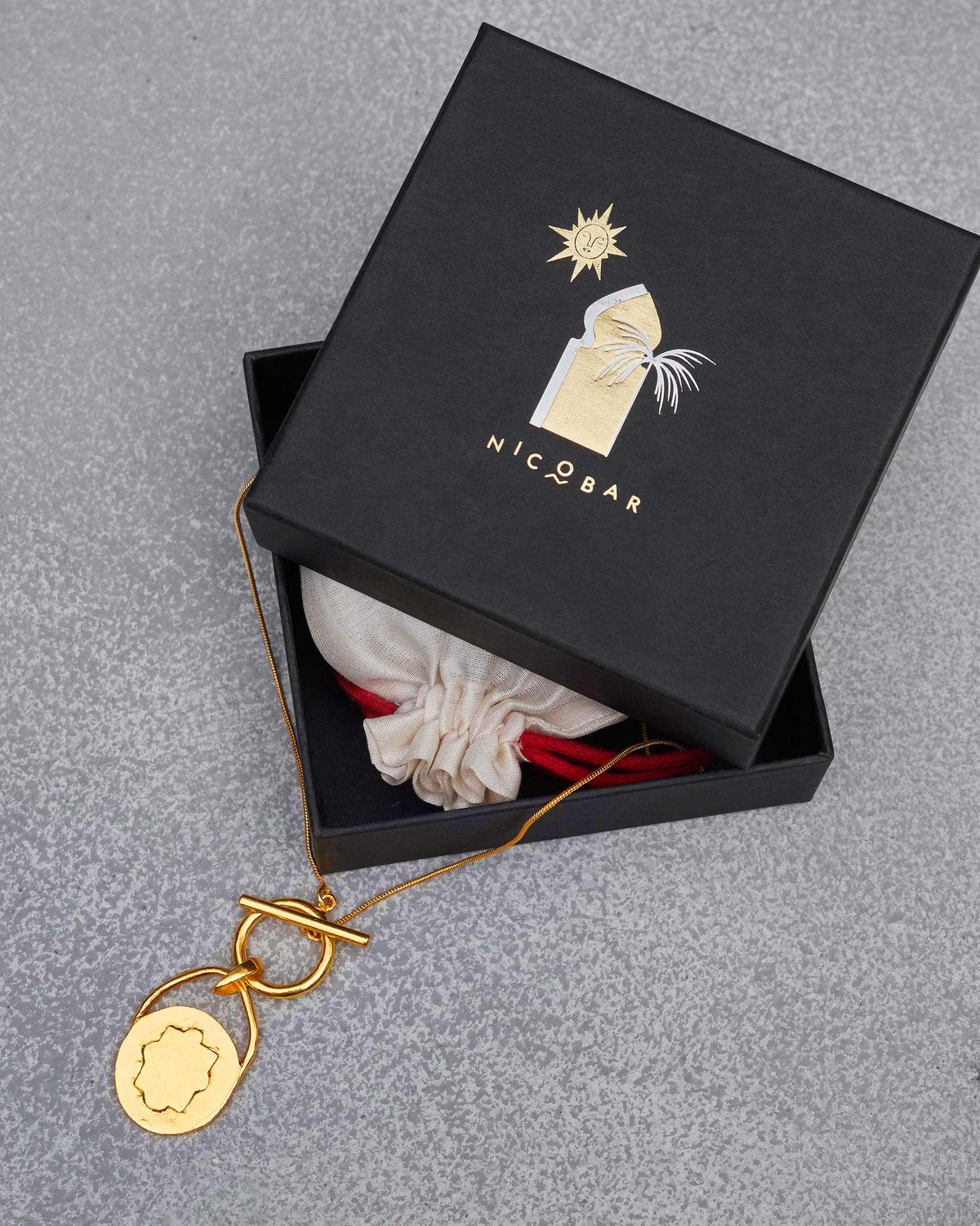 Gold Stardrop Necklace with a medallion pendant laid beside a black Nicobar gift box.
