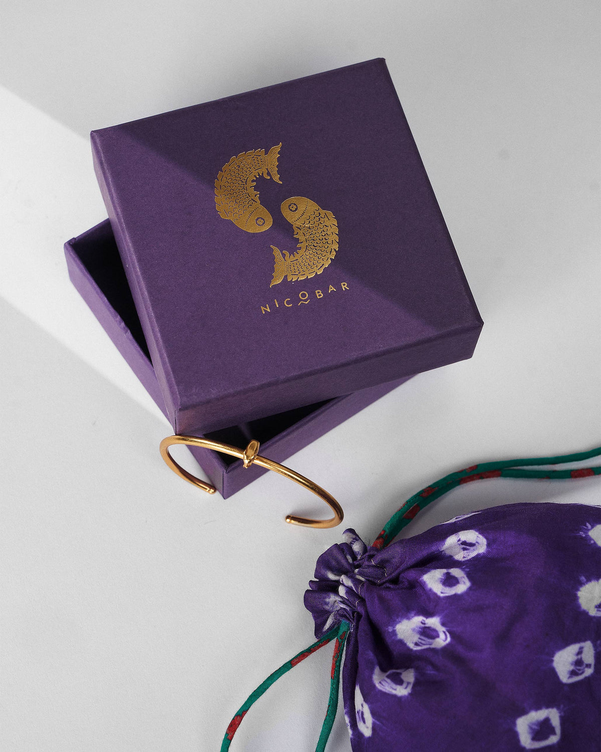 Gold haathi cuff beside a purple Nicobar gift box.