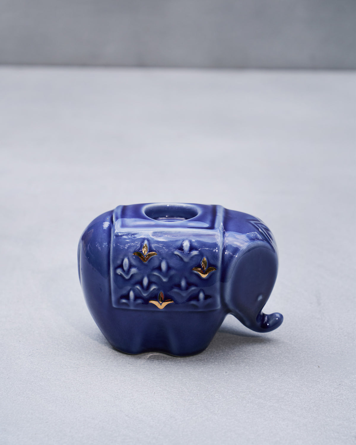 Side view of a blue glazed Tusker elephant votive with gold leaf accents.