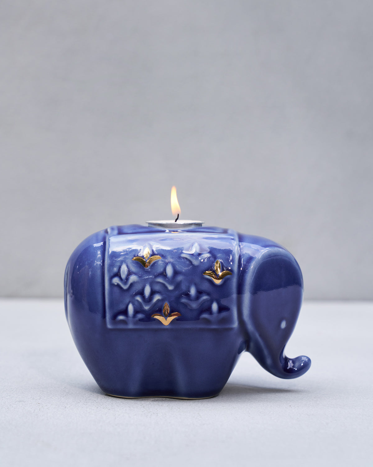 Blue Tusker votive holding a lit tealight on its embossed gold saddle.