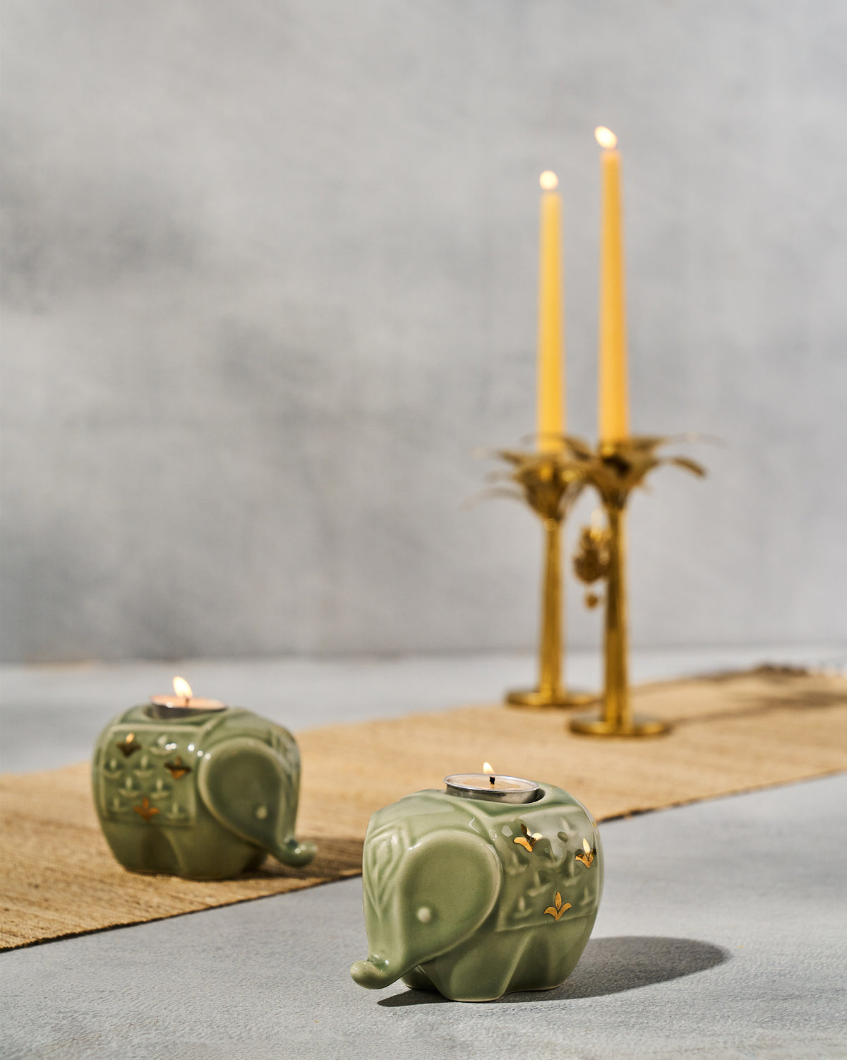 Lit Tusker sage green elephant votives on a woven runner.