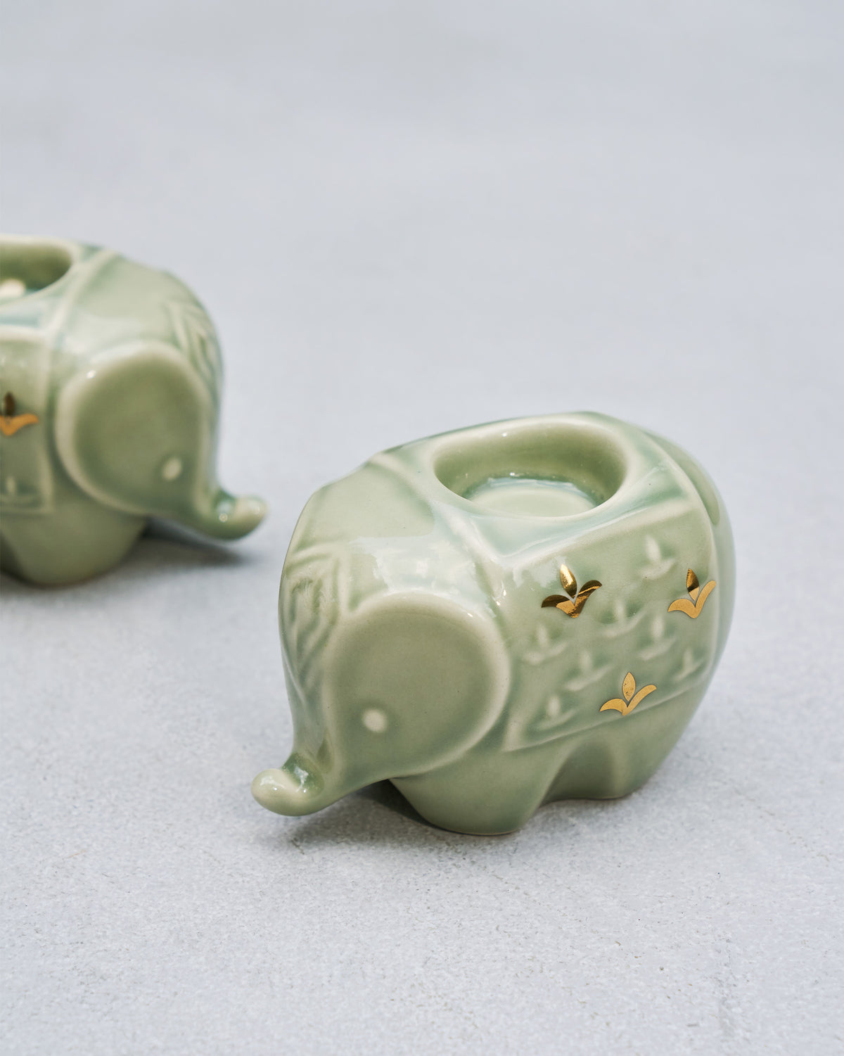 Close-up of a Tusker celadon elephant votive with gold accents.