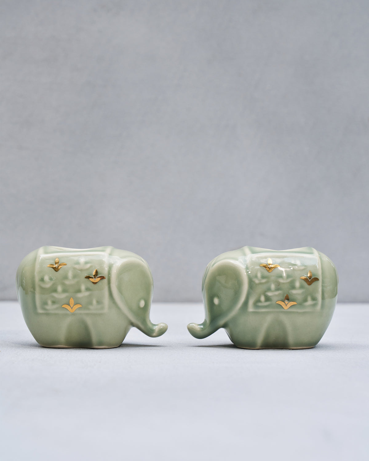 Pair of Tusker sage green elephant votives with gold motifs.