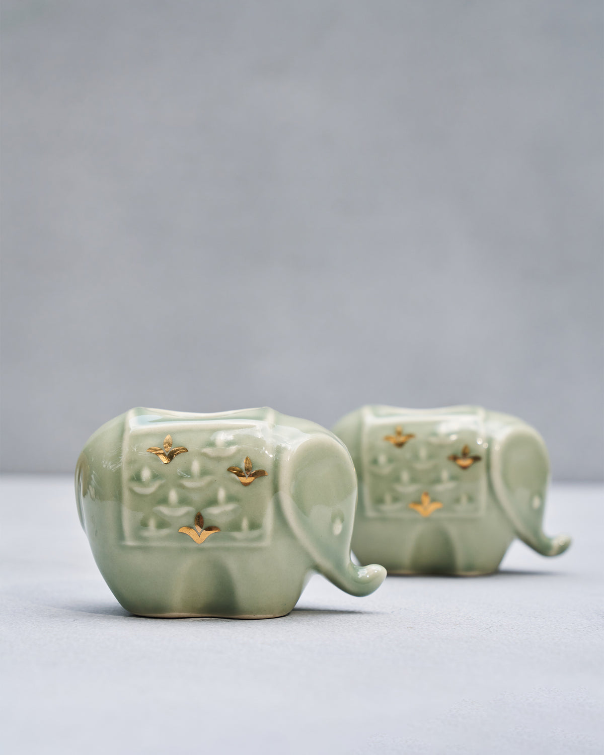 Tusker celadon elephant votives with gold diya accents.