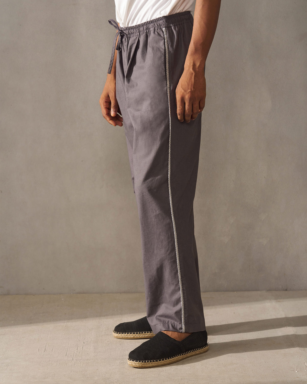 Side view of charcoal Tom Trousers showing white piping along the side seam.