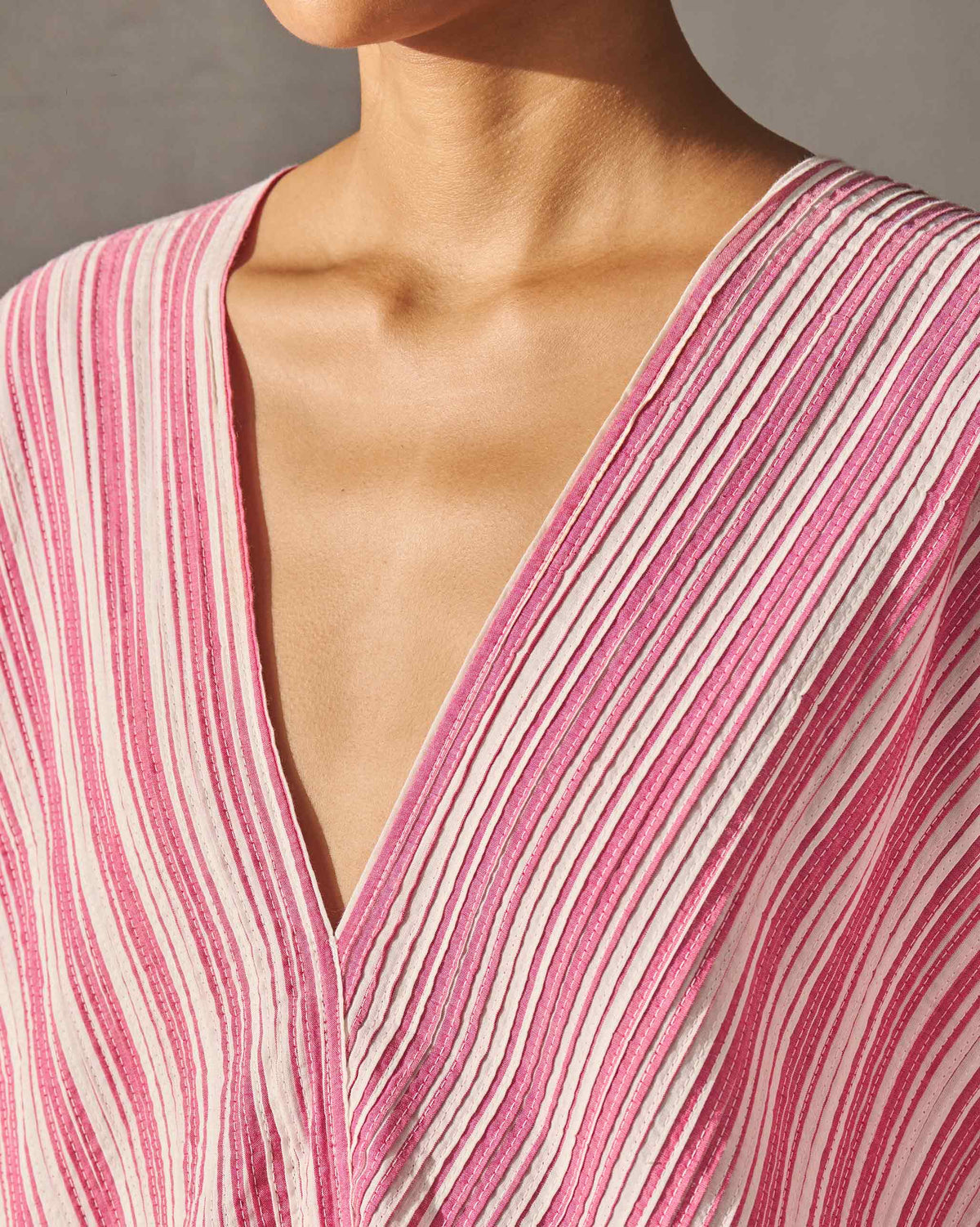 Close-up of the V-neck of a Sarai Kaftan with its pleated fuchsia and ivory stripes.