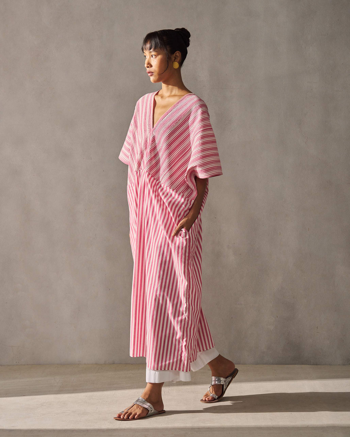 Side view of a Sarai Kaftan in fuchsia and ivory stripes, with a hand in its side pocket.