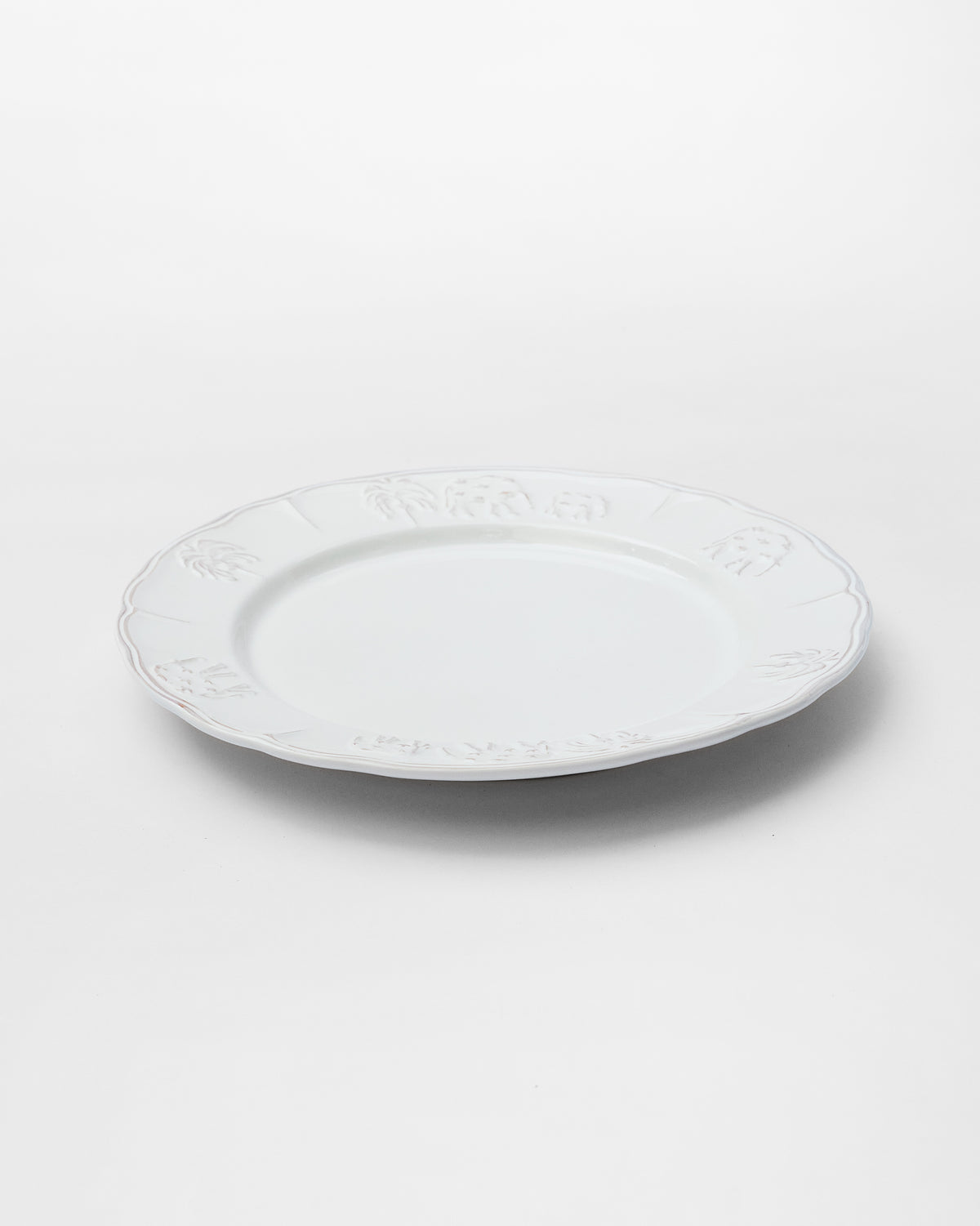 Ele Palm Dinner Plate at an angle, showing its scalloped rim with embossed motifs.
