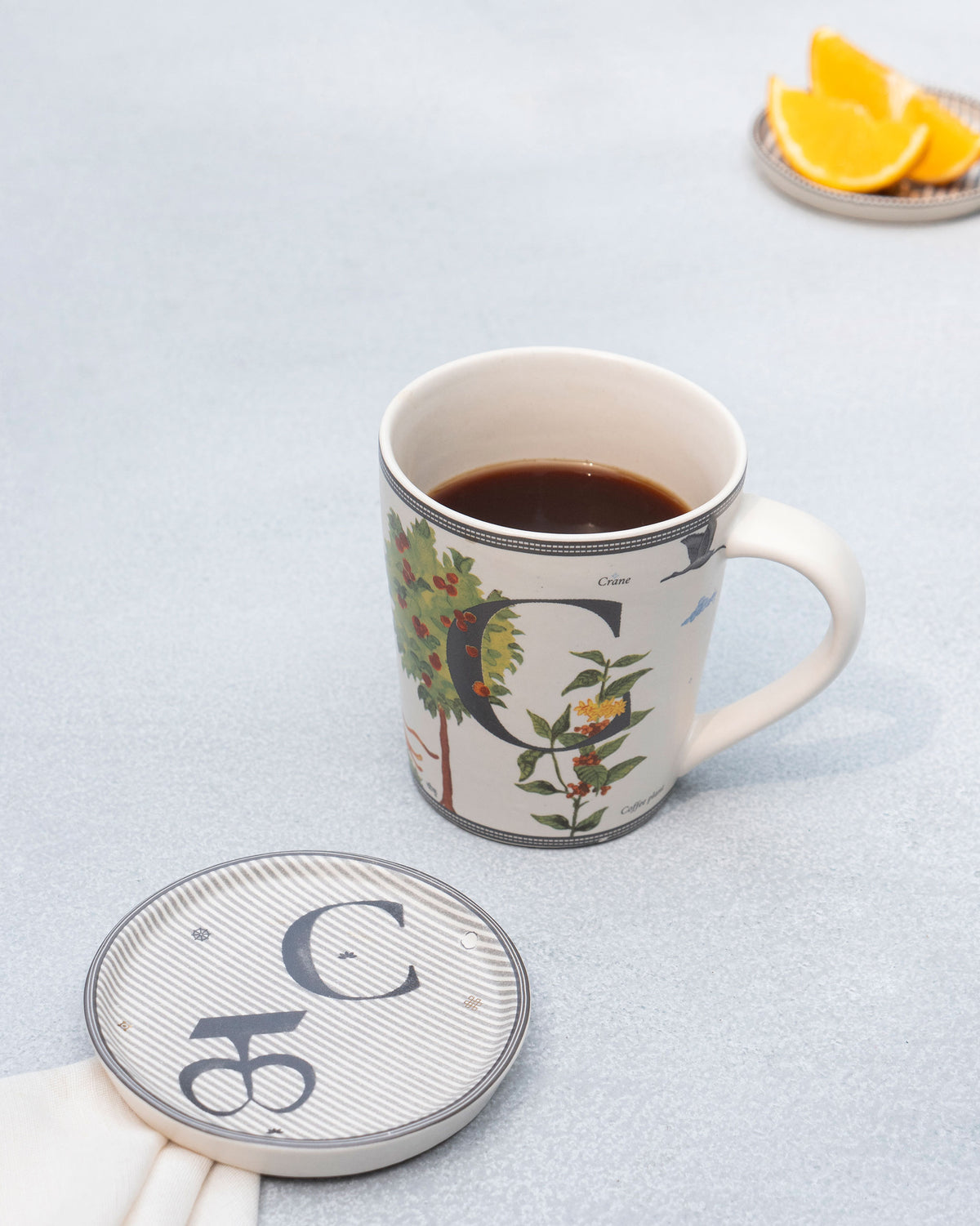 Letter C Alphabet mug filled with coffee beside its striped coaster.
