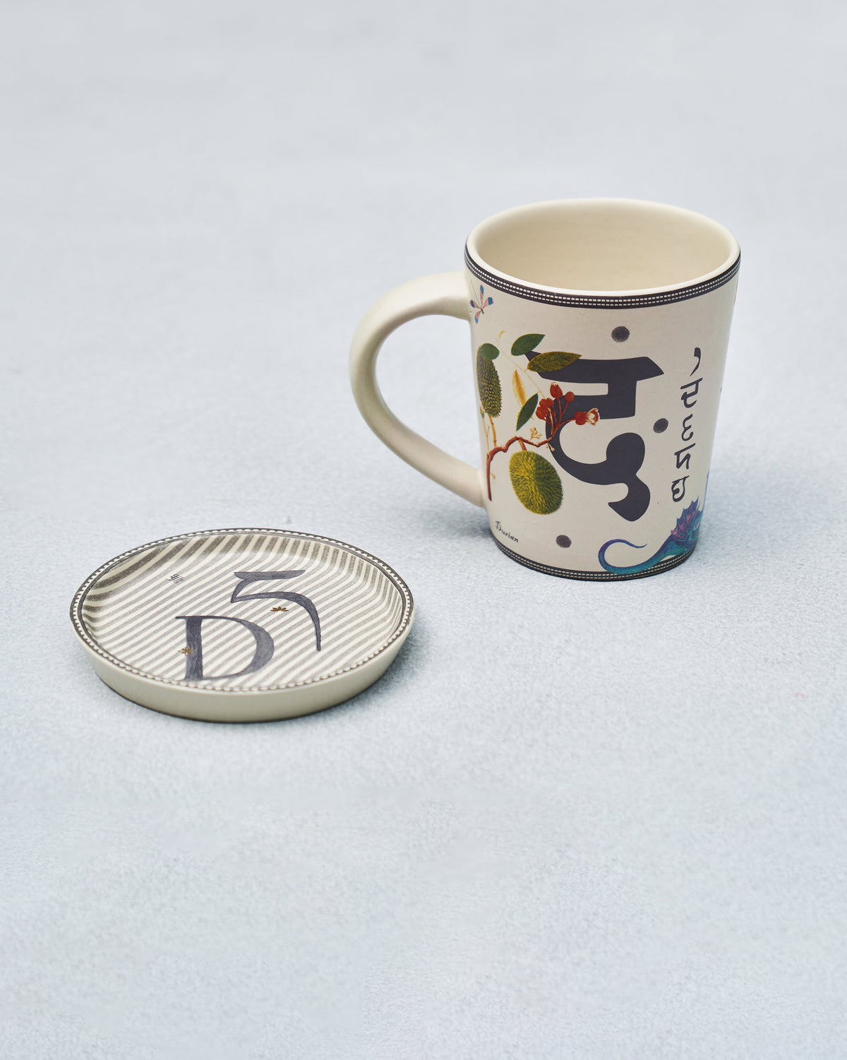 Alphabet mug showing Indian script and jackfruit beside the D coaster.