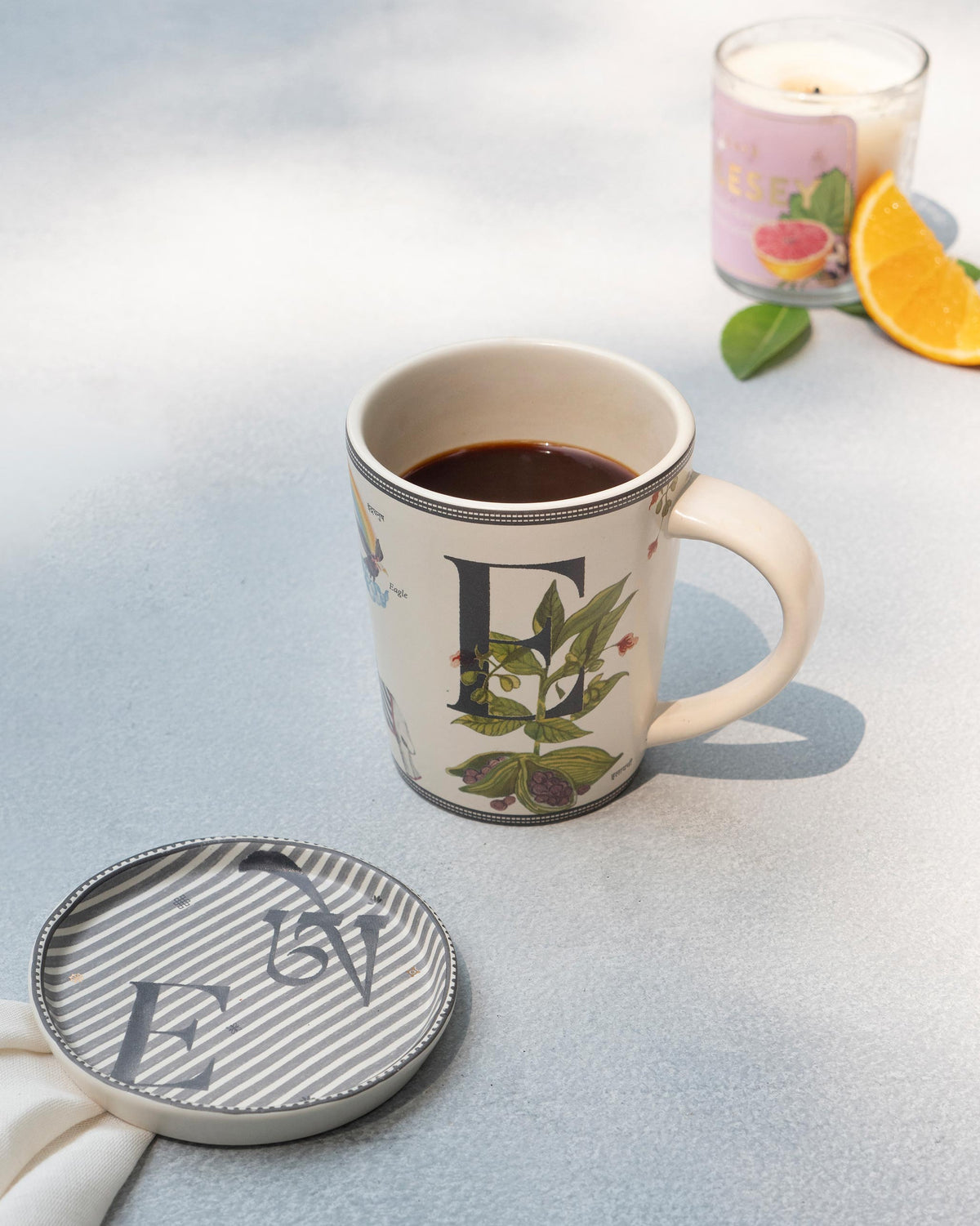 E Alphabet mug filled with coffee beside a matching letter E coaster.