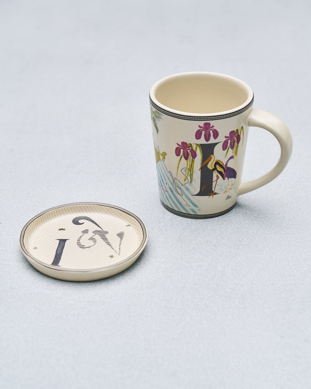 Cream I alphabet mug with iris and stork beside matching coaster.