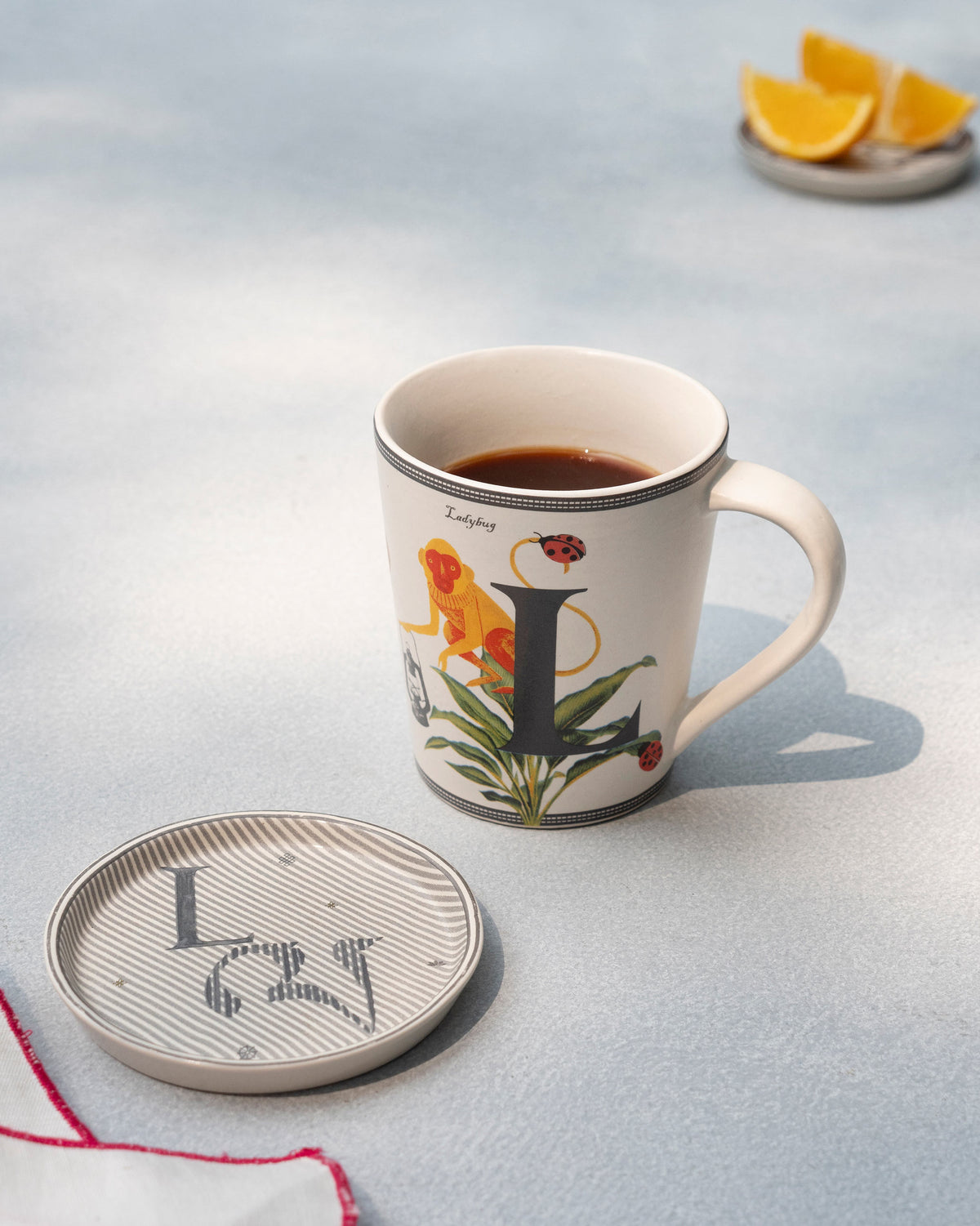 Cream L alphabet mug with coffee beside a matching coaster.