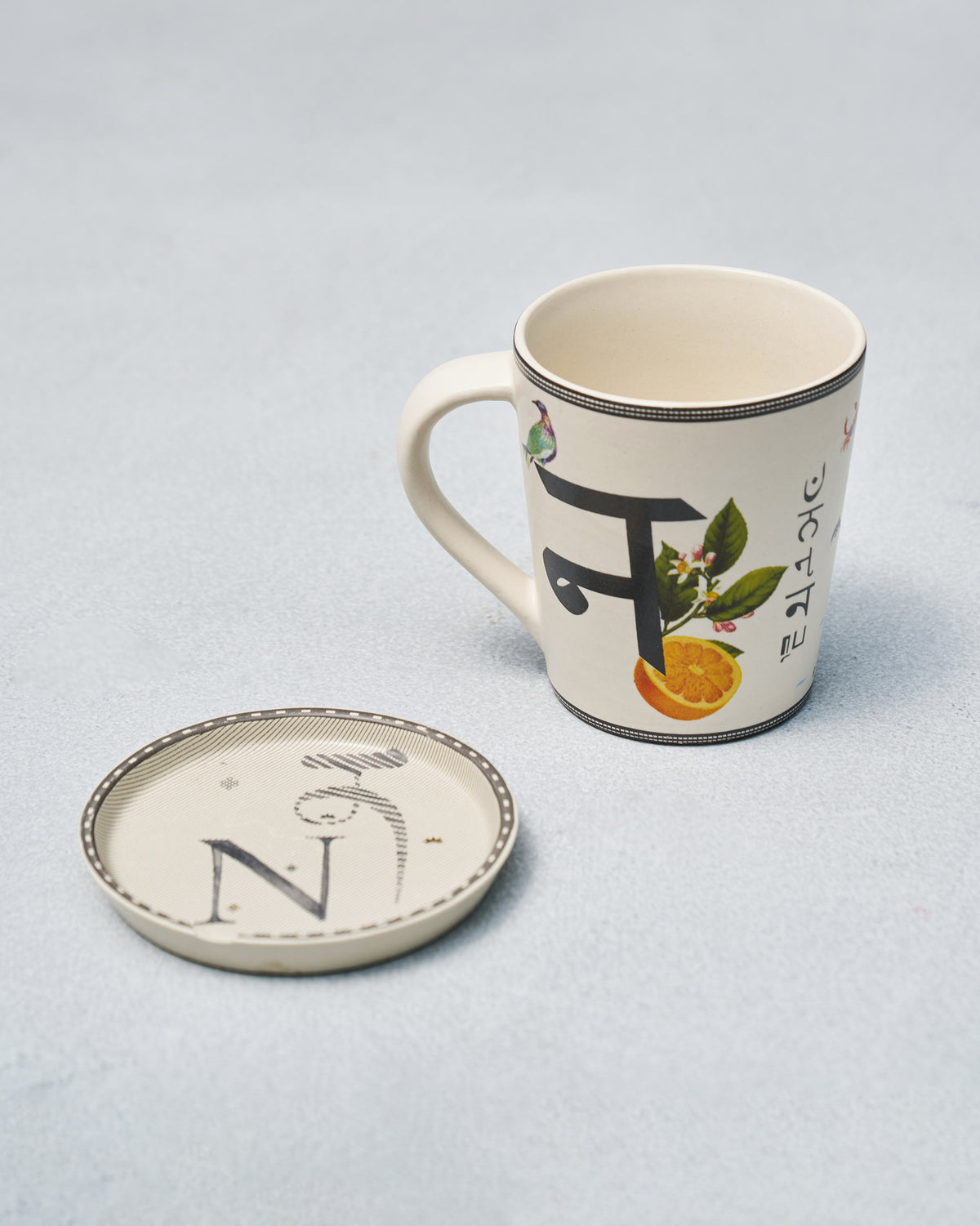 N alphabet mug showing Devanagari न with a bird and orange, beside the N coaster.