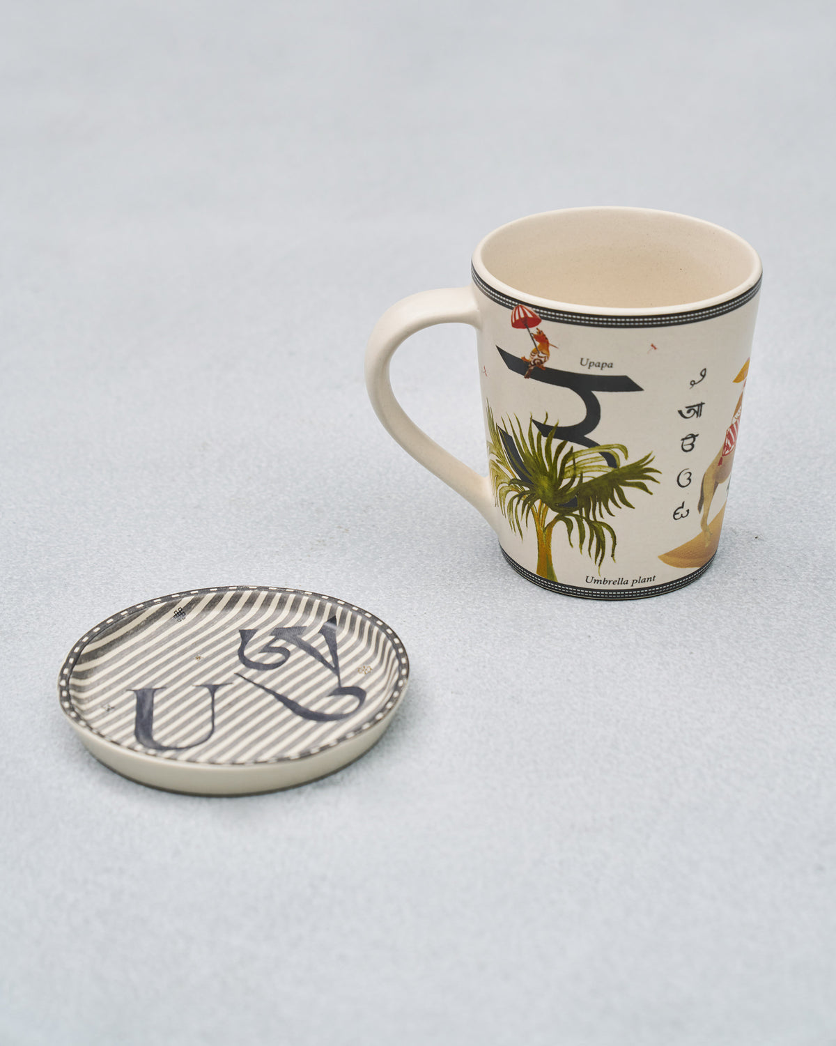 U alphabet mug showing Indian scripts beside its striped coaster.