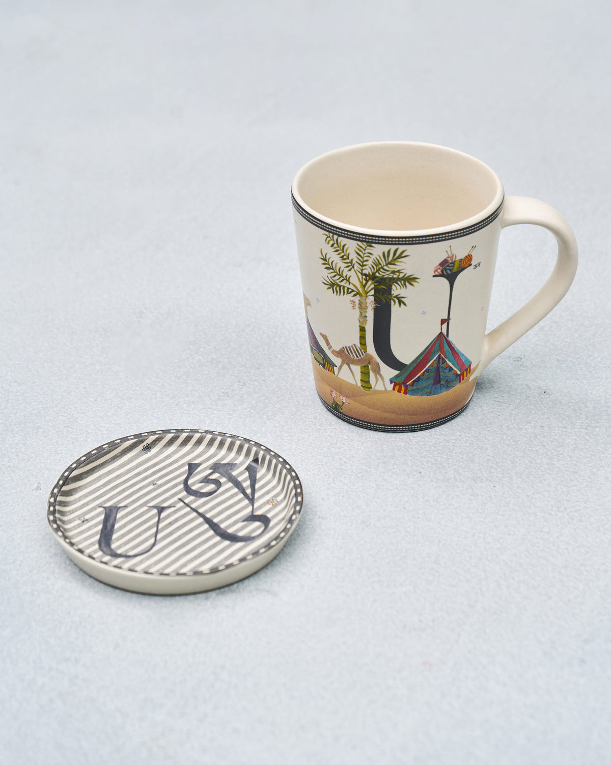 U alphabet mug with desert motif beside its striped U coaster.