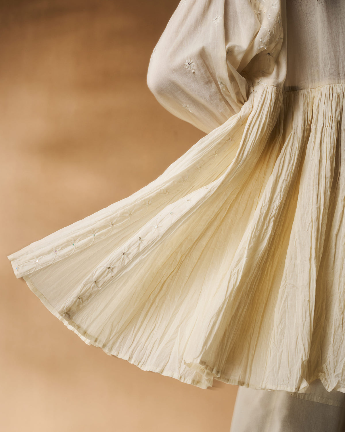 Close-up of the pleated hem and floral embroidery on an ivory chikankari Taabir top.