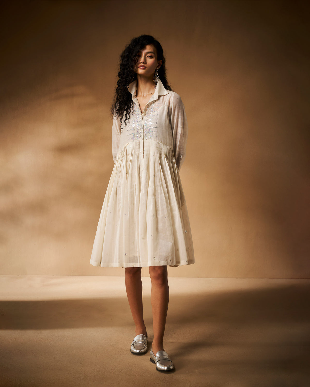 Person wearing an ivory Qurbat dress with silver sequin embroidery on the bodice.