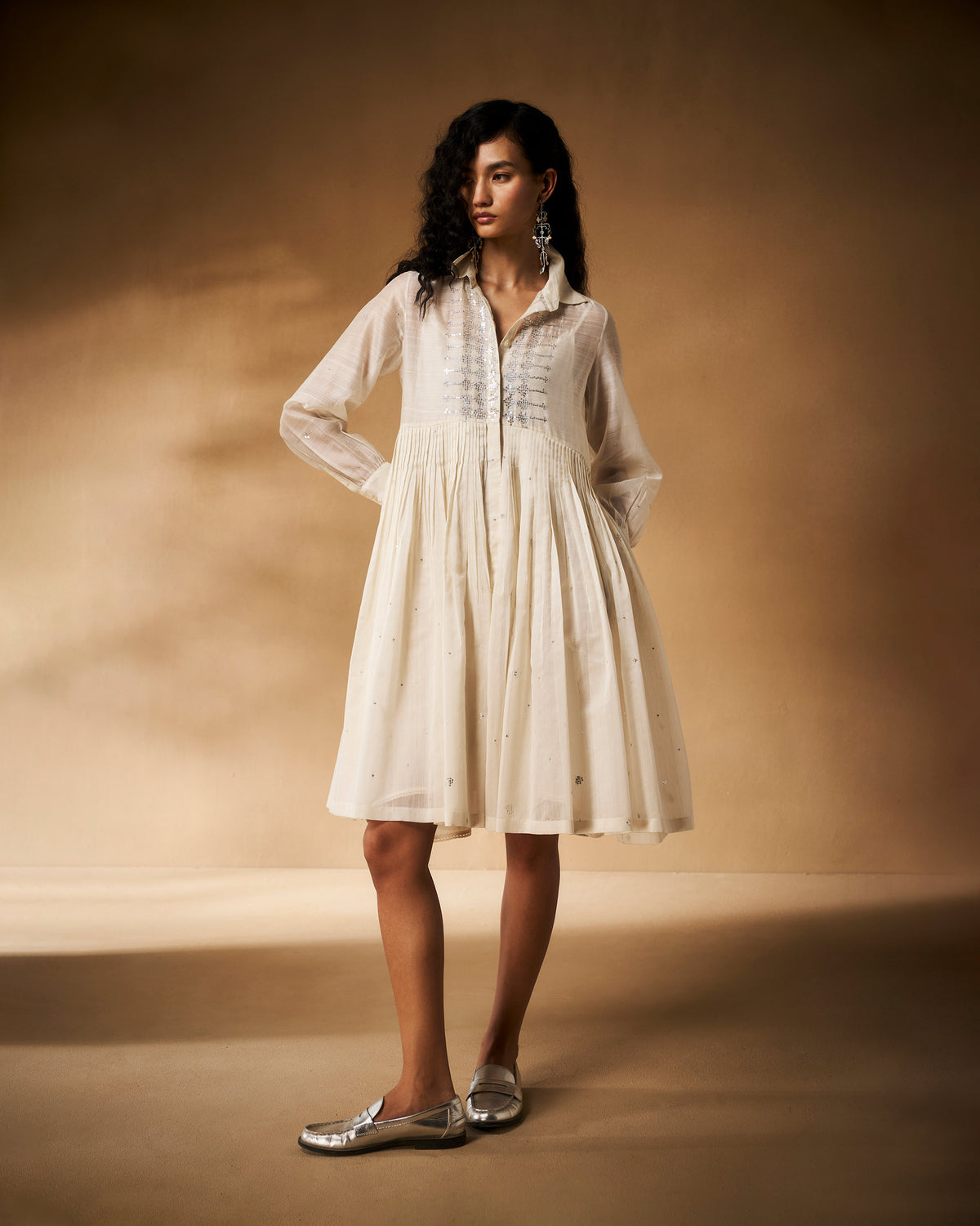 Person wearing an ivory Qurbat shirt dress with a gathered skirt.
