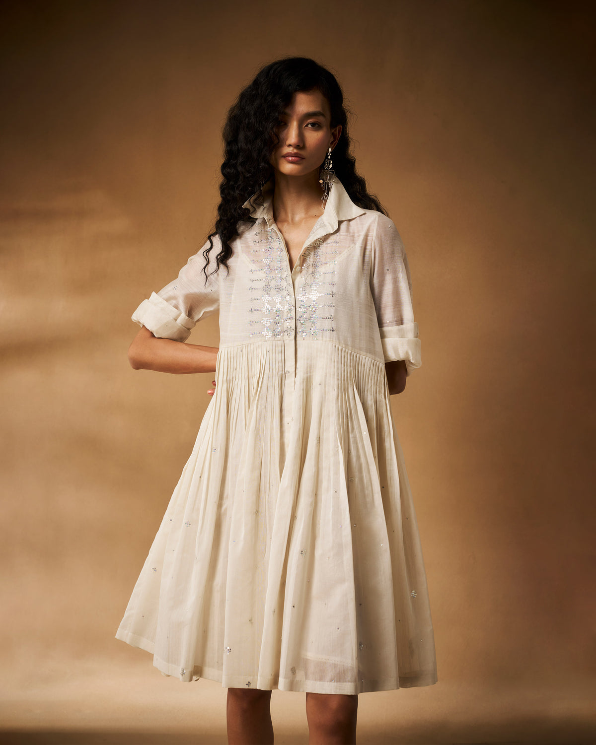 Person wearing an ivory Qurbat dress with a pin-tucked flared skirt.