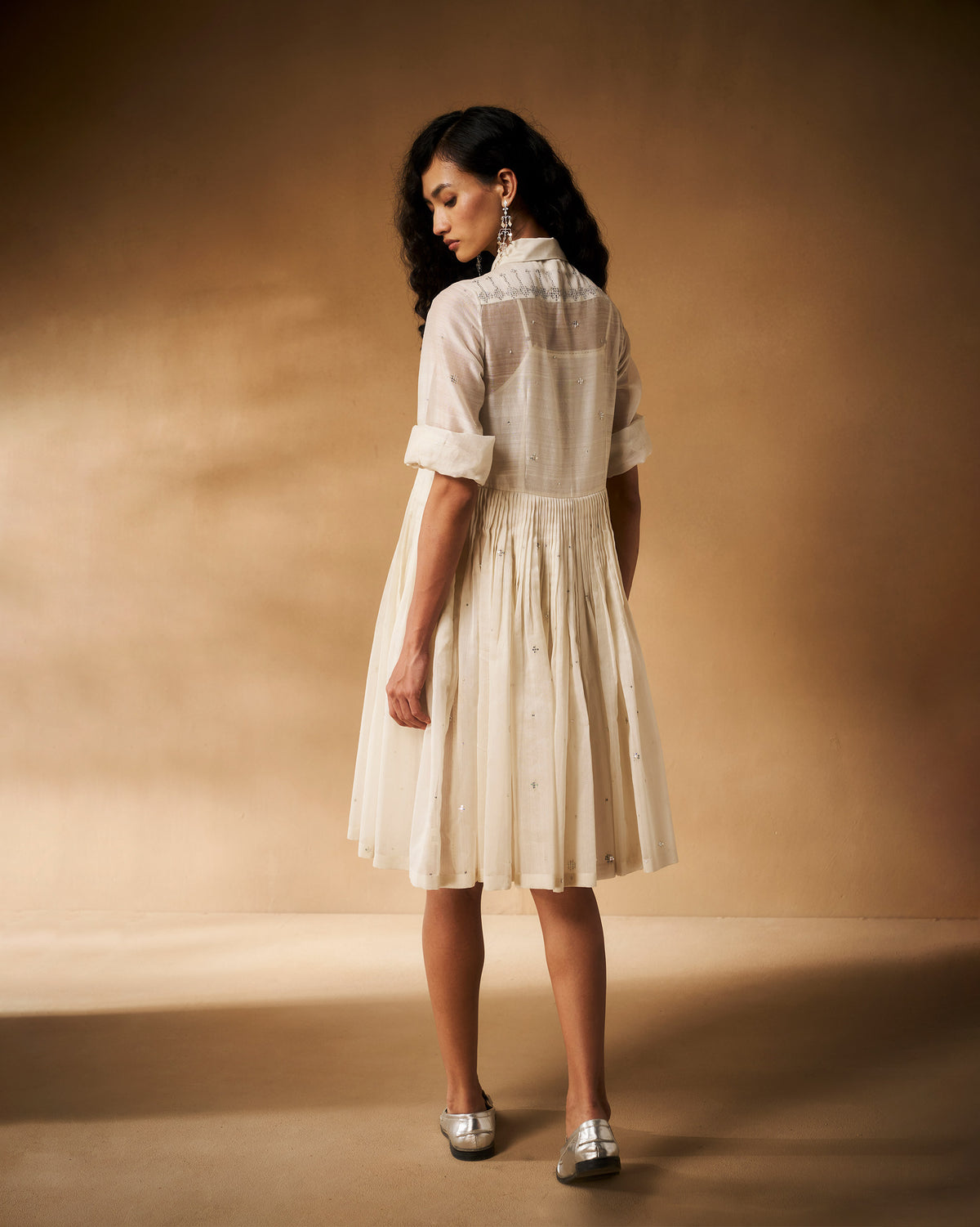 Back of an ivory Qurbat dress with a pleated skirt and silver accents.