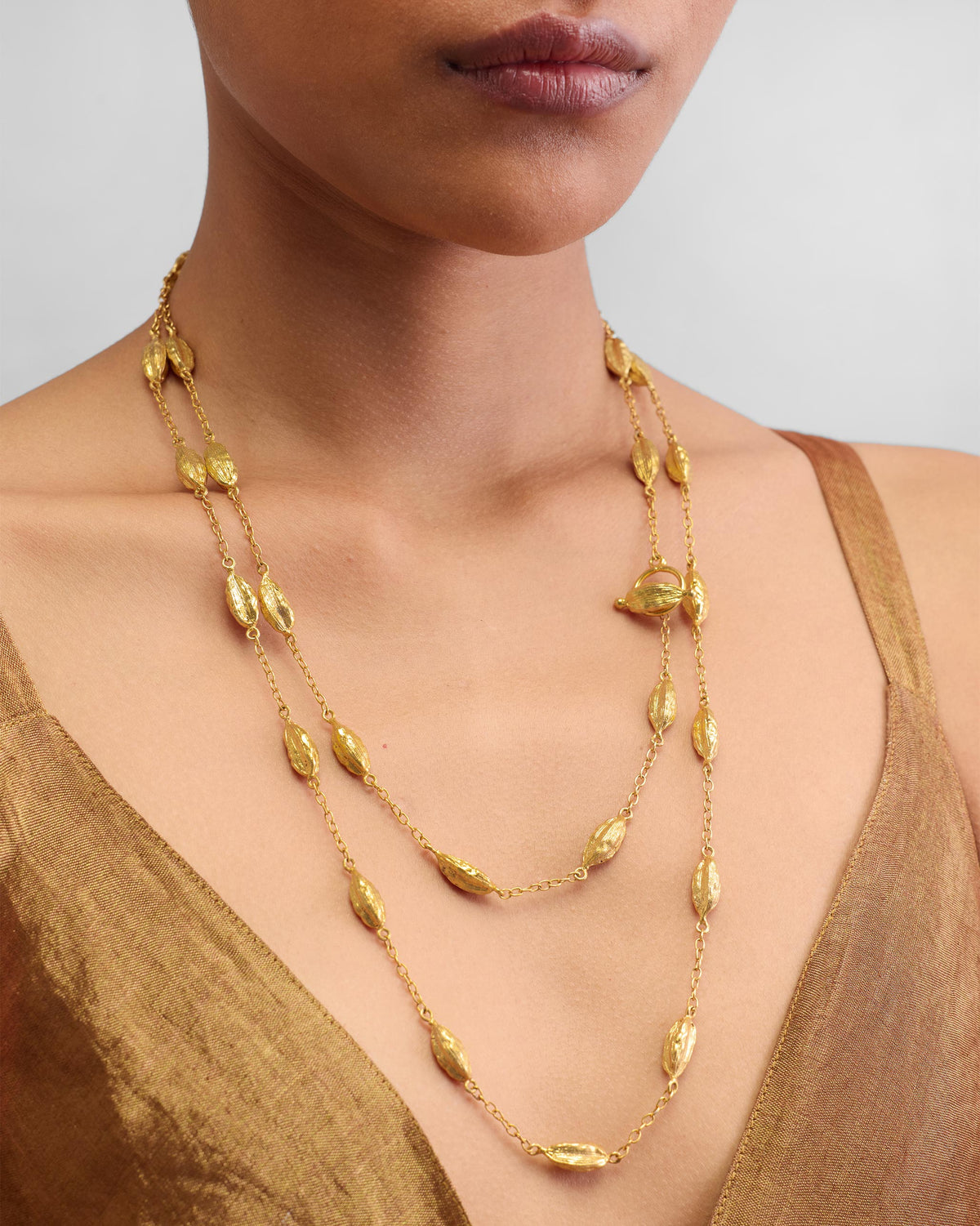 Person wearing a long gold Shanti Necklace with textured beads.