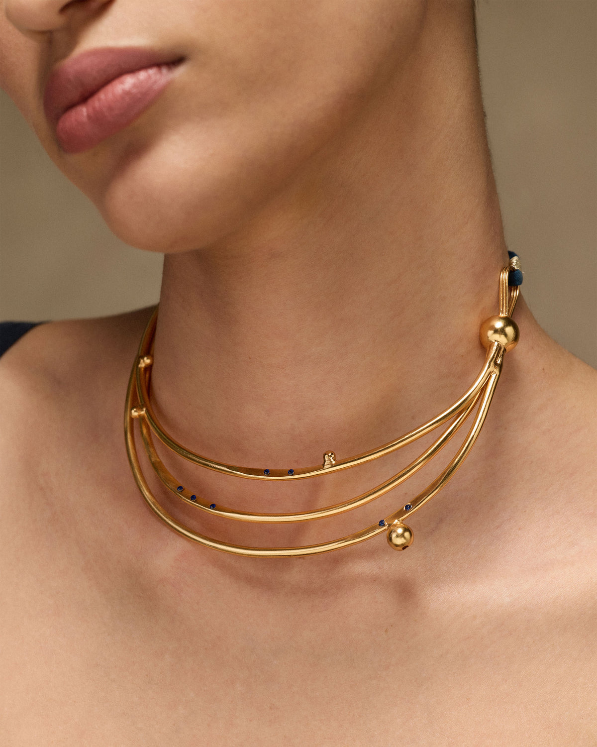 Gold Celestial choker with three crescent tiers worn on a navy cord.