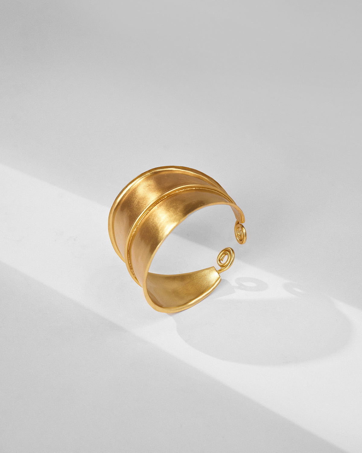 Side view of a gold rays cuff with coiled open ends.