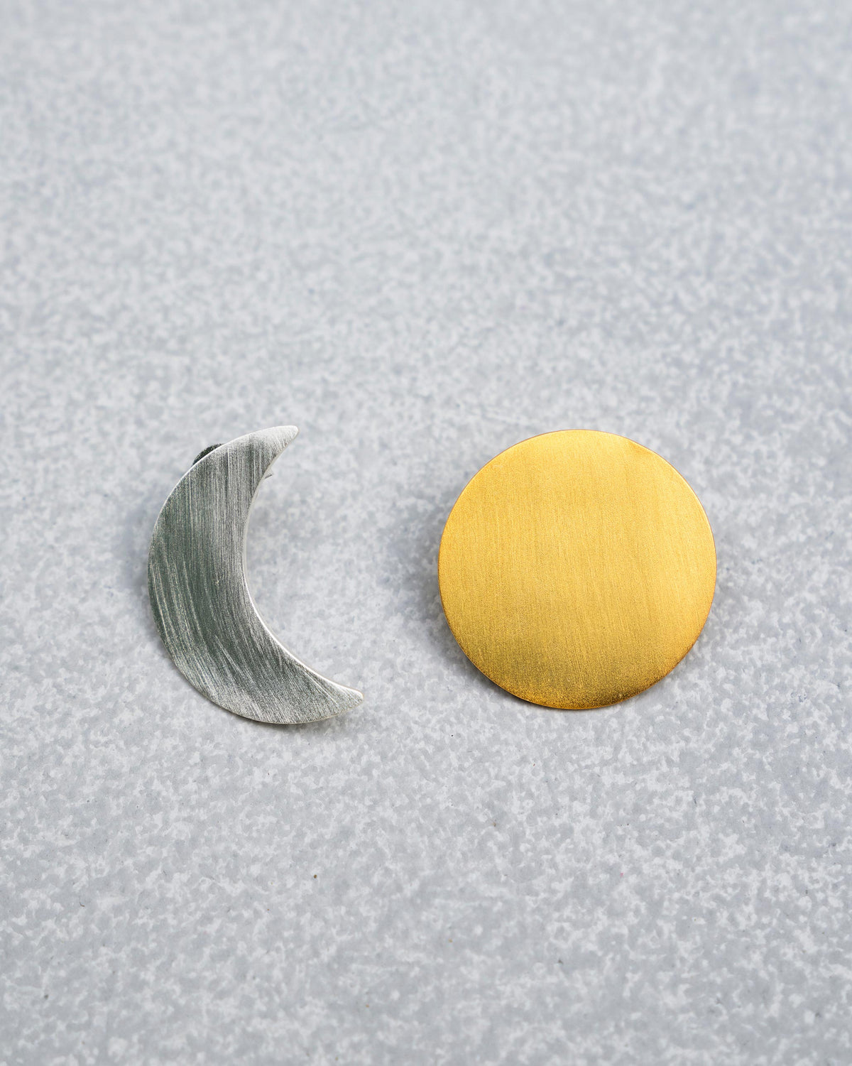 Pair of gold and silver Sun Moon stud earrings laid flat.
