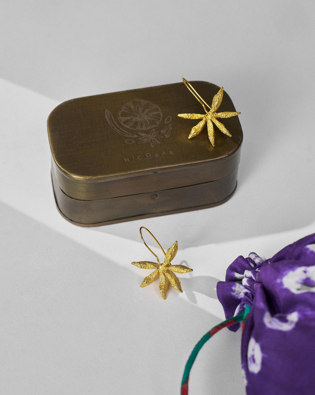 Gold Star Anise dangle earrings with a Nicobar gift tin.