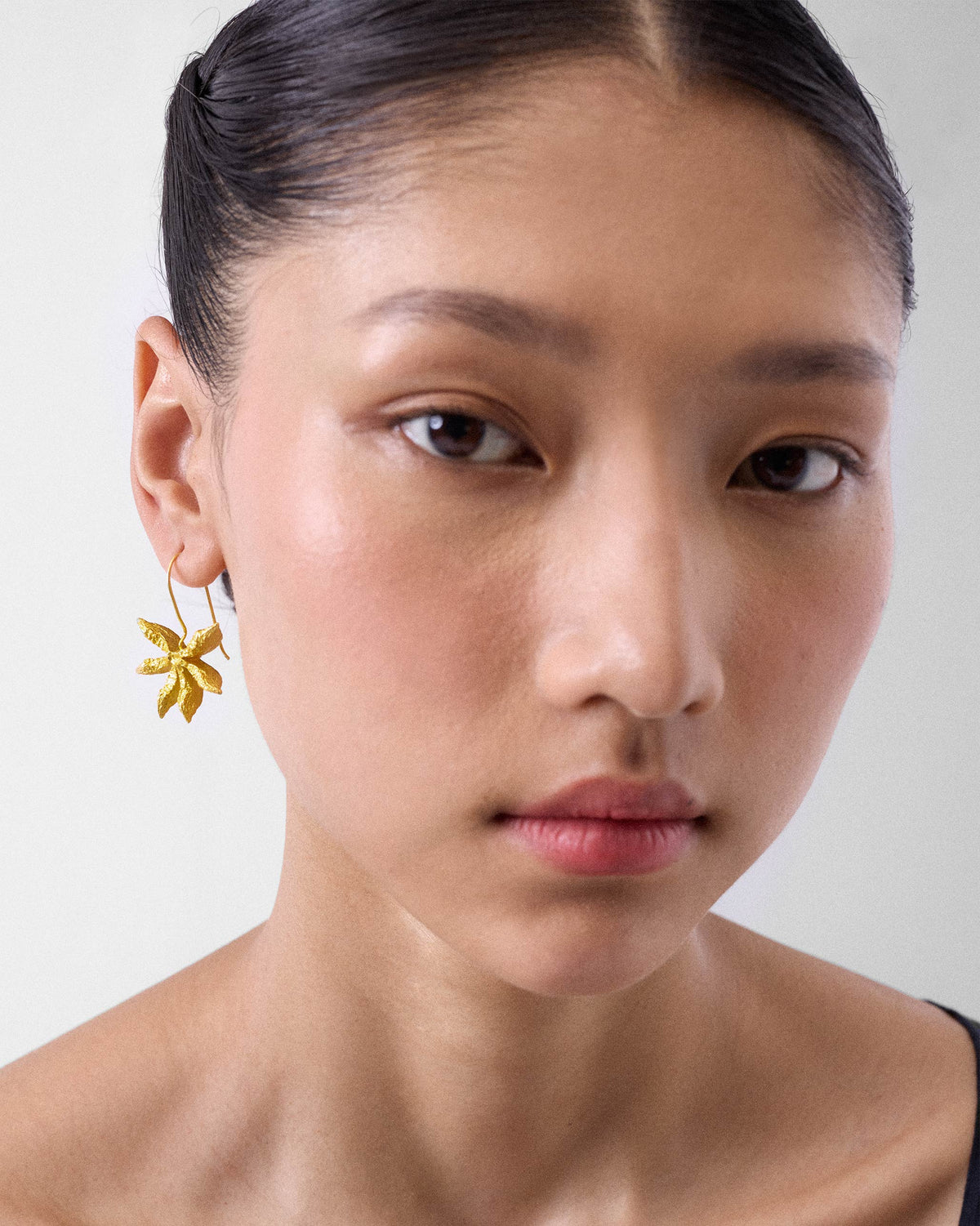 Person wearing gold Star Anise dangle earrings.