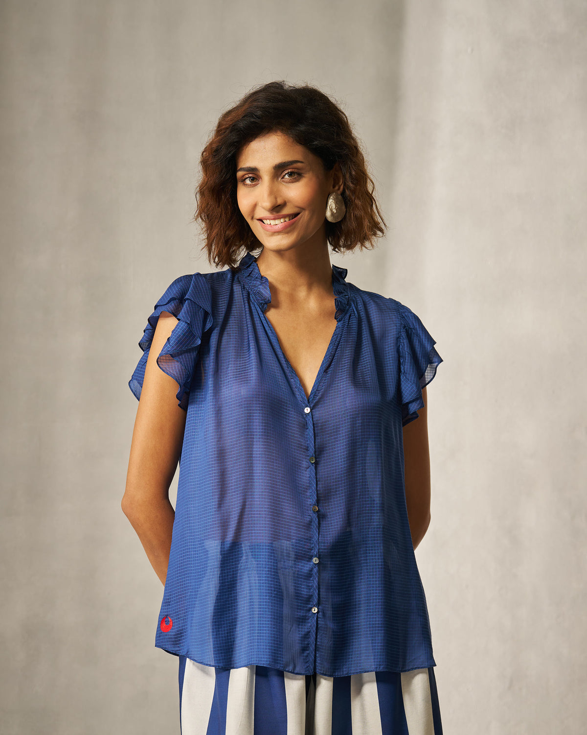 Person wearing a blue check shirt with a ruffled collar and tiered sleeves.