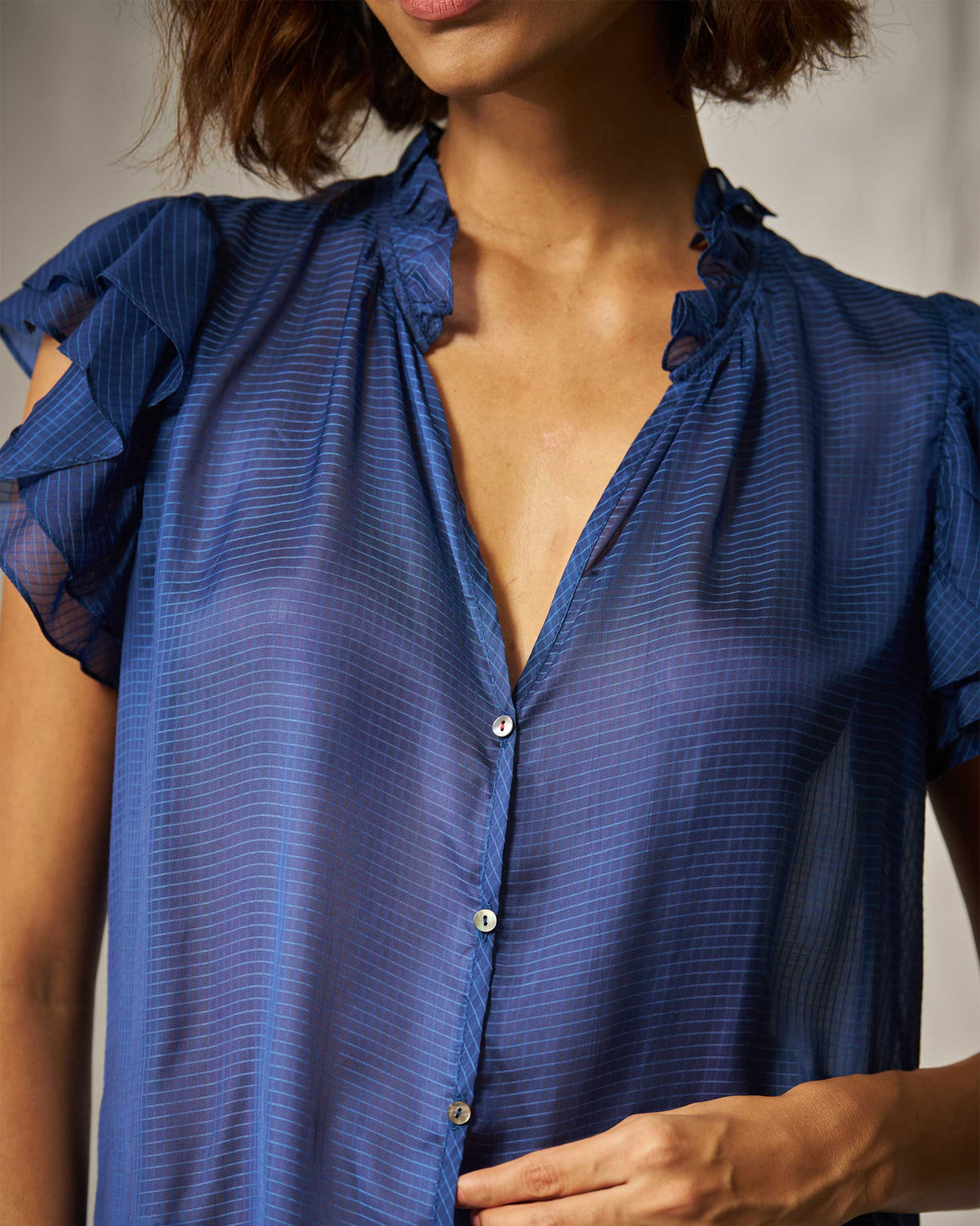 Close-up of a blue check shirt with a ruffled V-neck and pearl buttons.