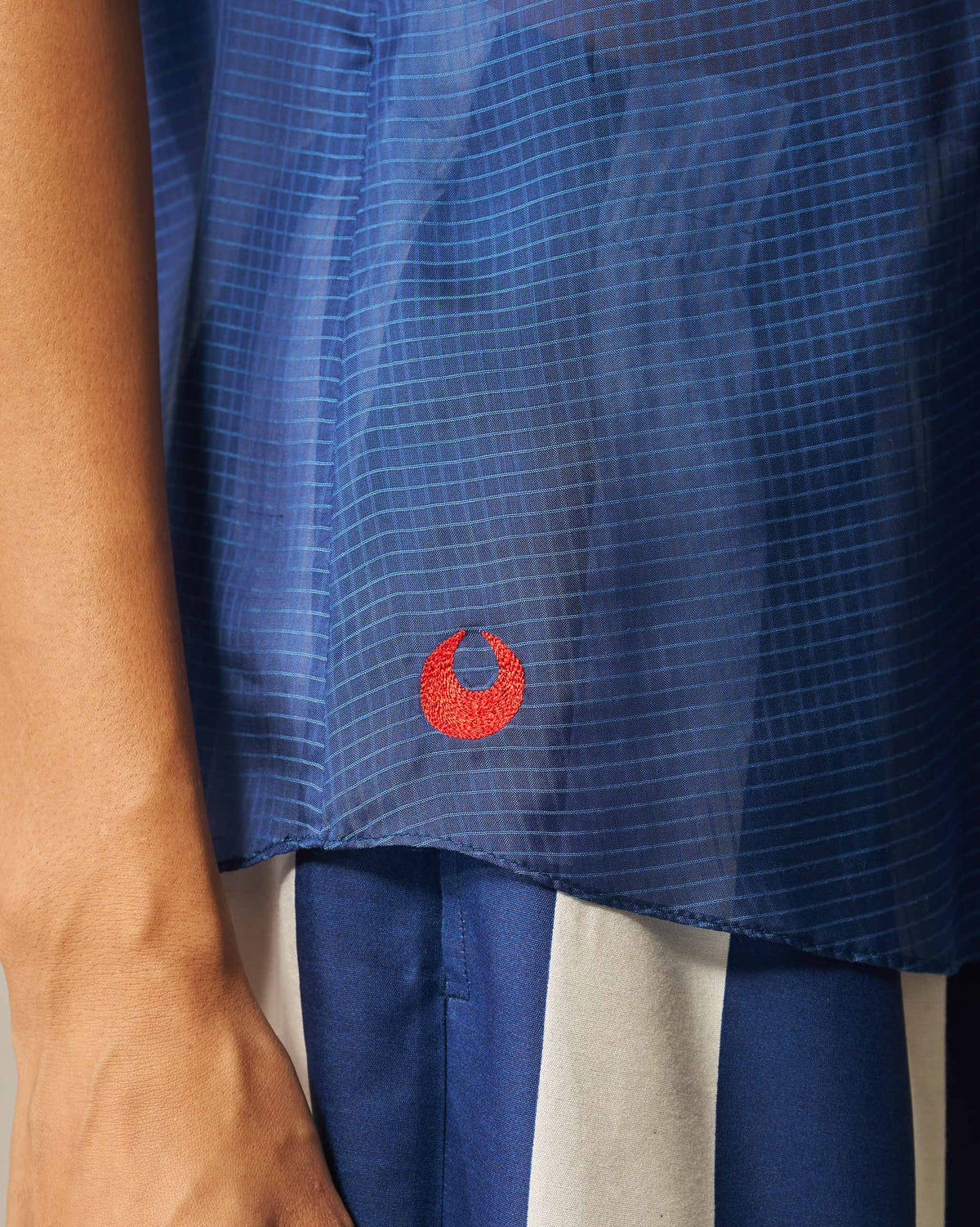 Close-up of a blue check shirt hem with a small red embroidered motif.