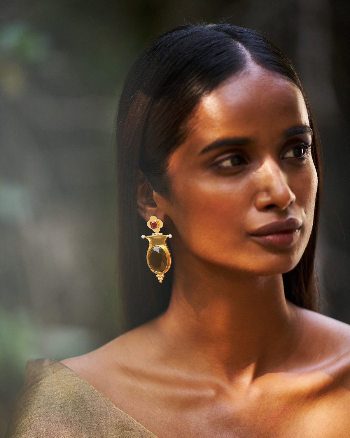 Person wearing gold eden drop earrings with amber glass and pearls.