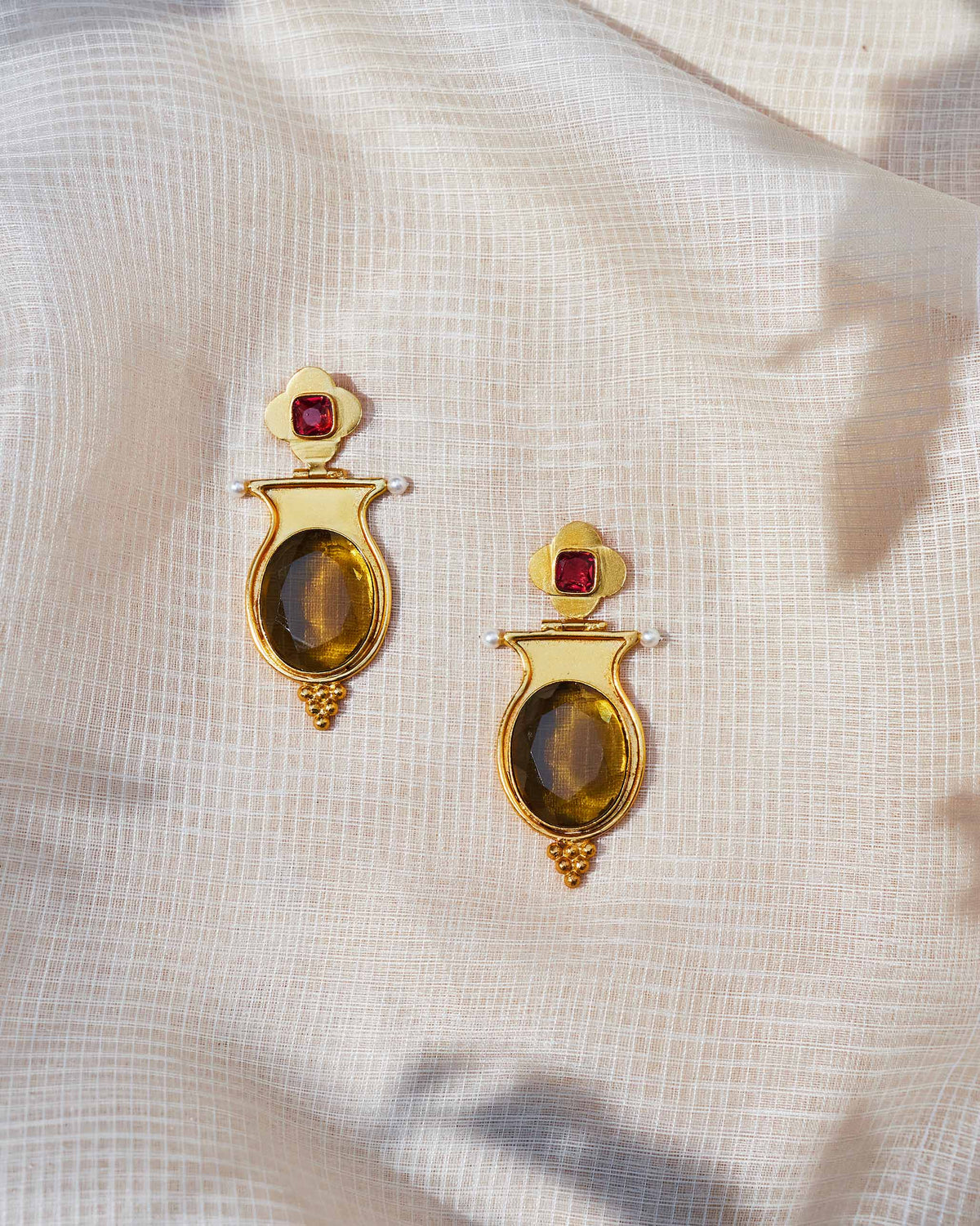 Pair of gold eden drop earrings with oval glass and pearls laid flat.