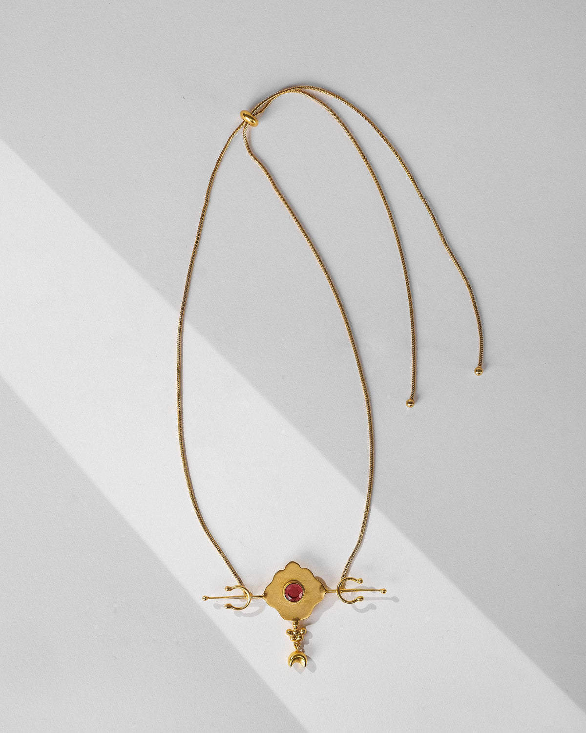 Gold Berber necklace laid flat with red glass pendant and slider closure.