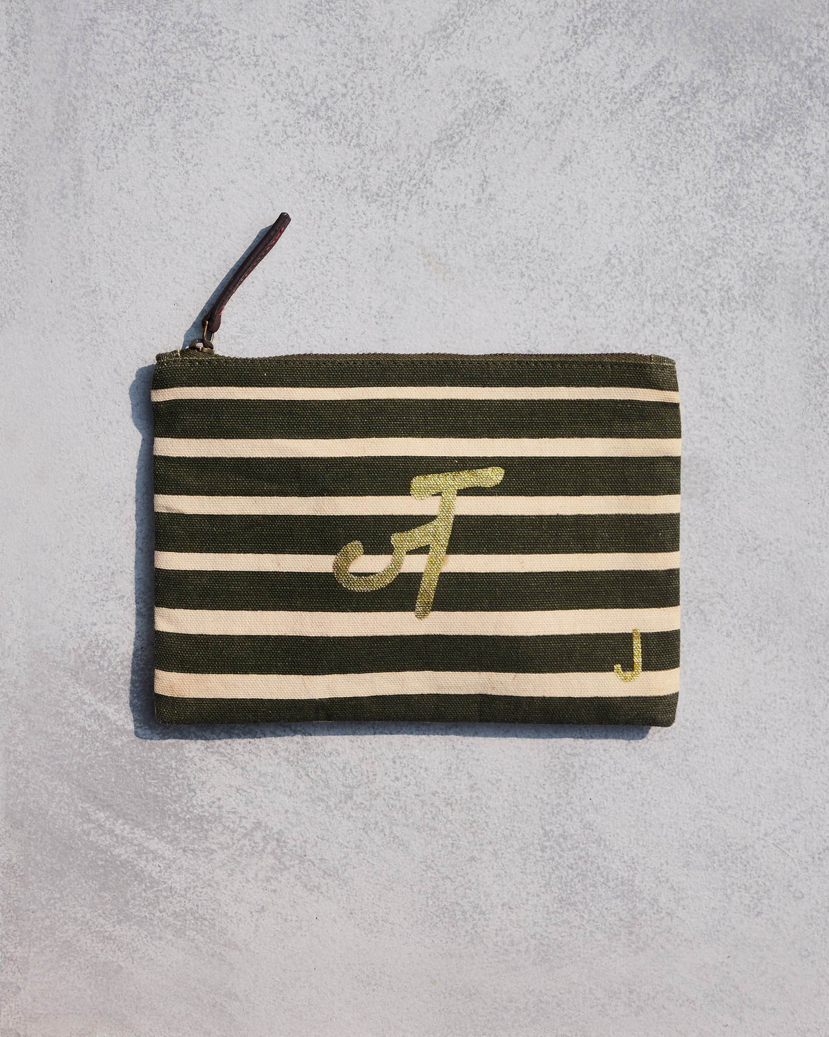 Alphabet J Pouch in olive and cream stripes with a gold script letter.