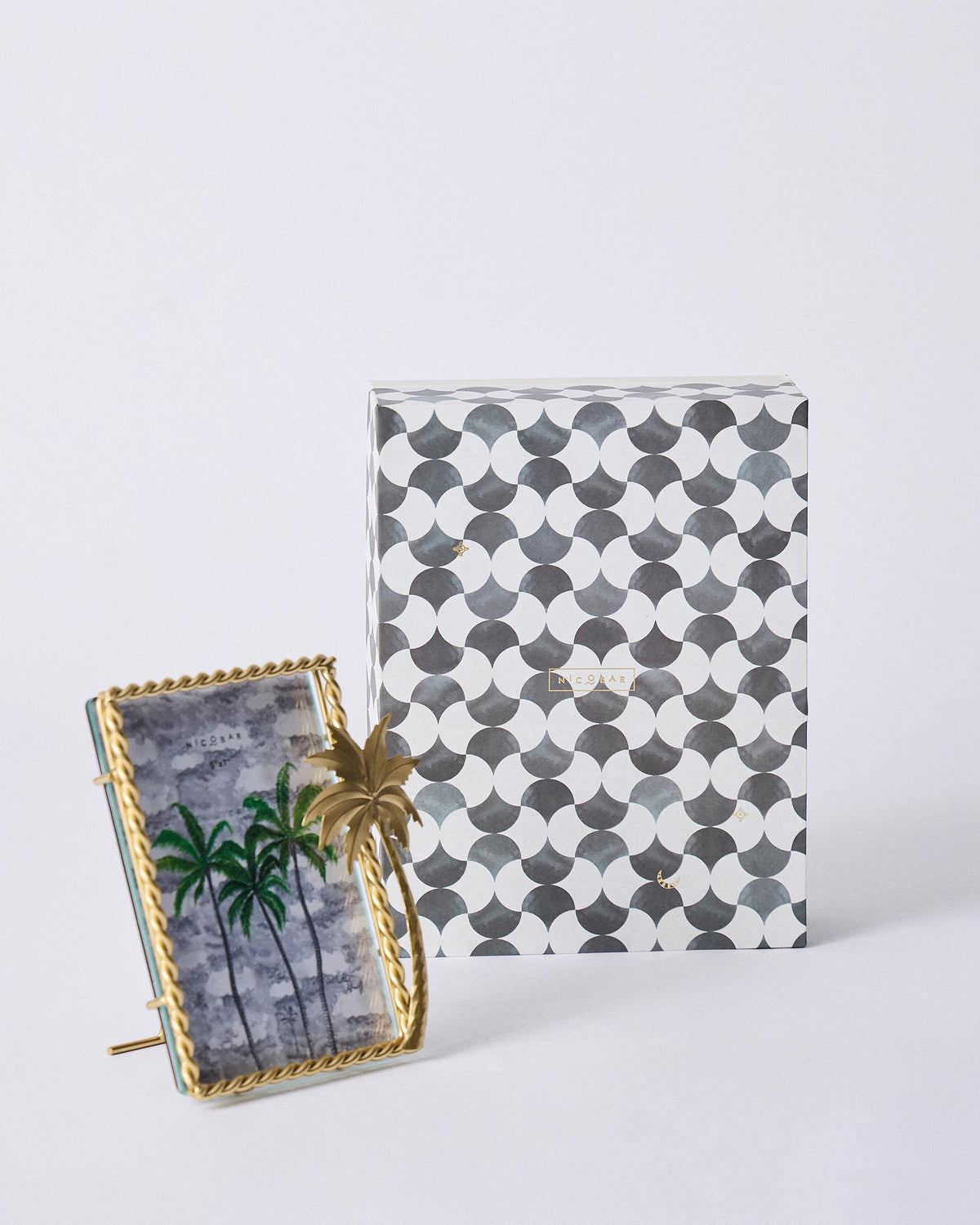 Gilded Palm photo frame standing in front of a patterned Nicobar gift box.