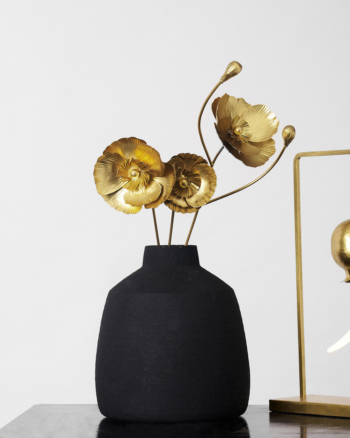 Matte black vase holding three gold Poppy accent stems with blooms and buds.
