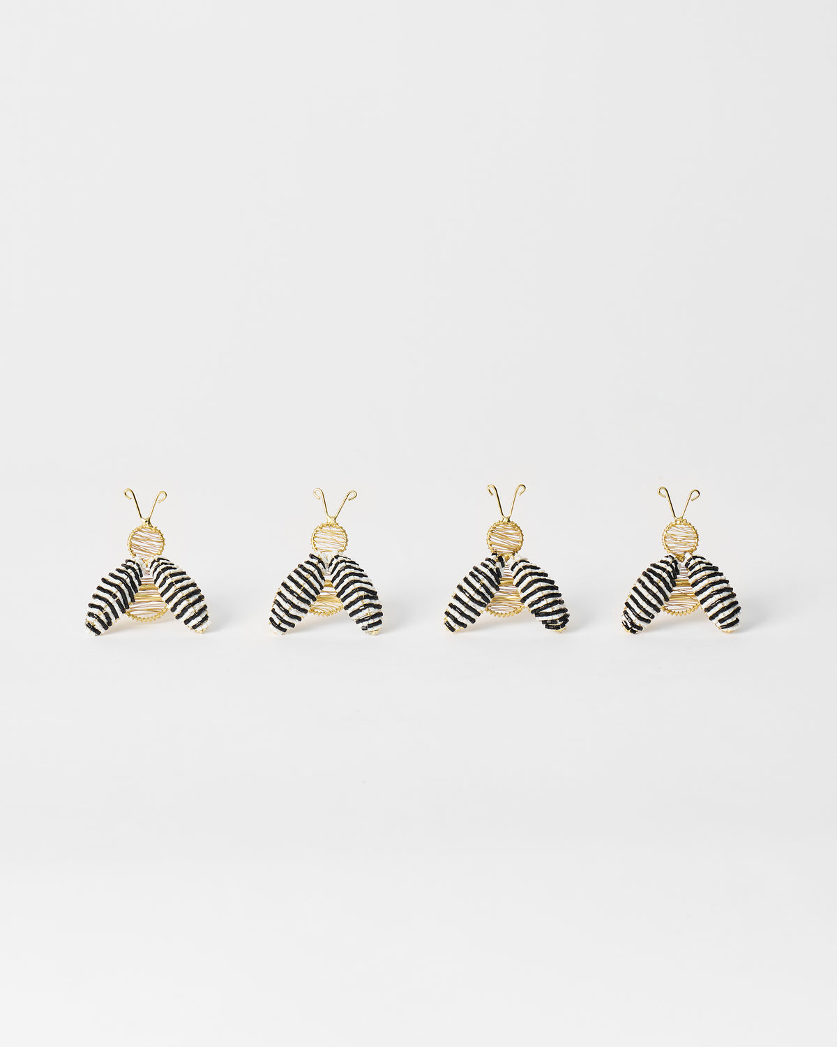 Set of four gold-wire bee napkin rings with black and white striped wings.