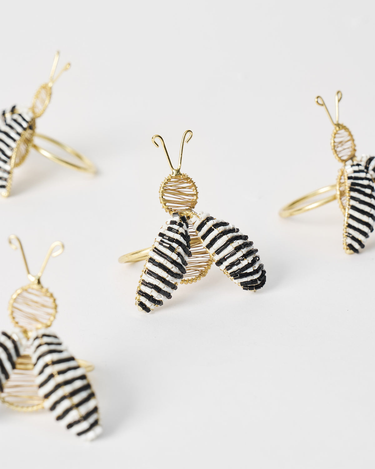 Gold-wire bee napkin rings with black and white striped wings clustered together.
