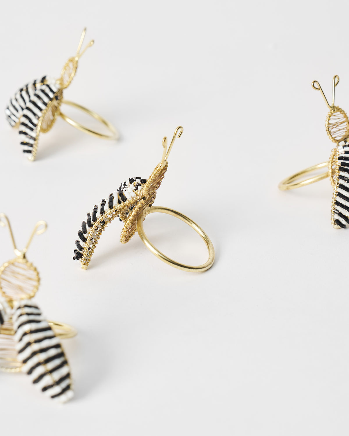 Four gold-wire bee napkin rings with black and white striped wings on white.